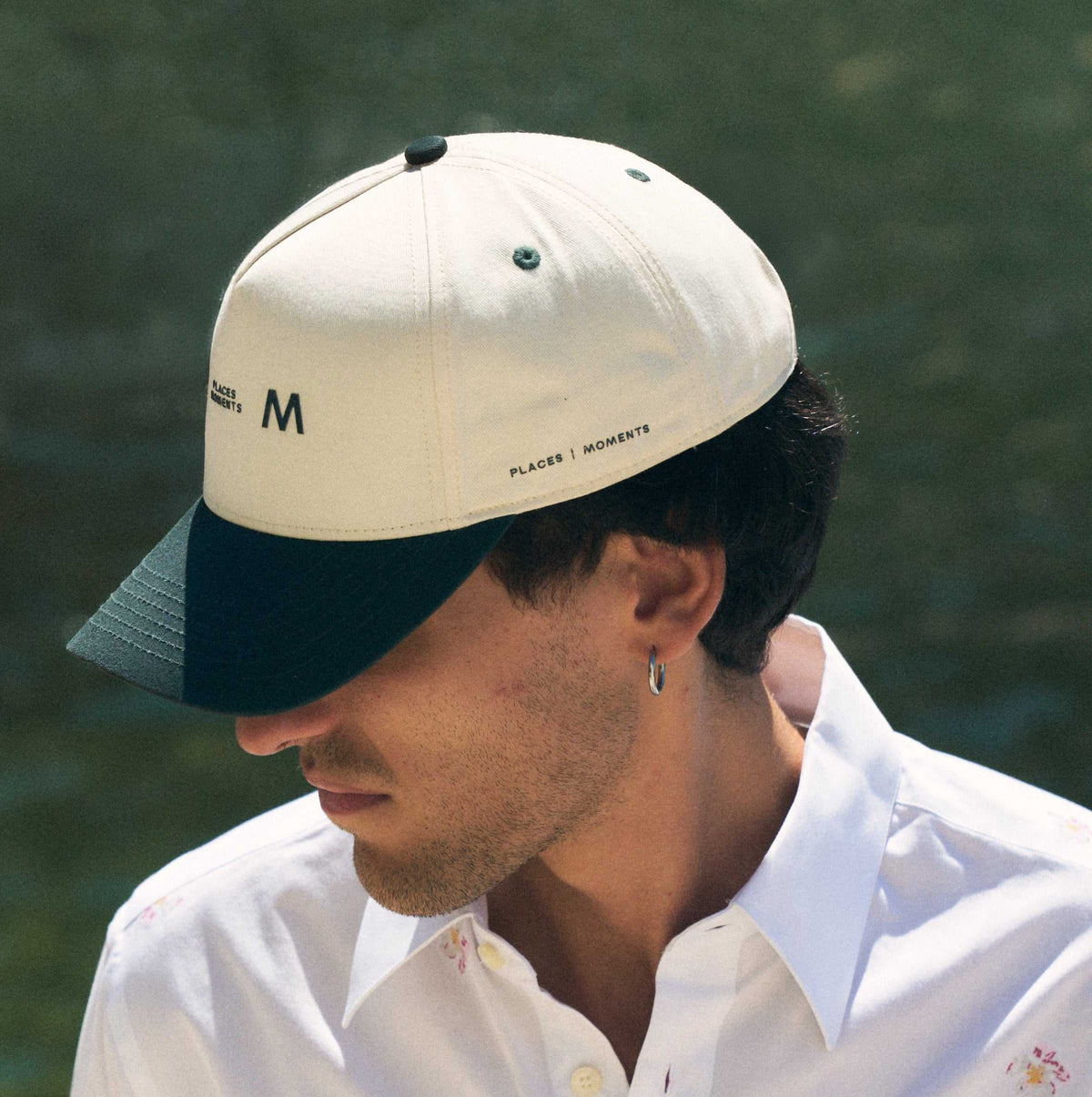 The Places Moments logo baseball cap in cream with a green brim, the top button and eyelets picked out in the same green.