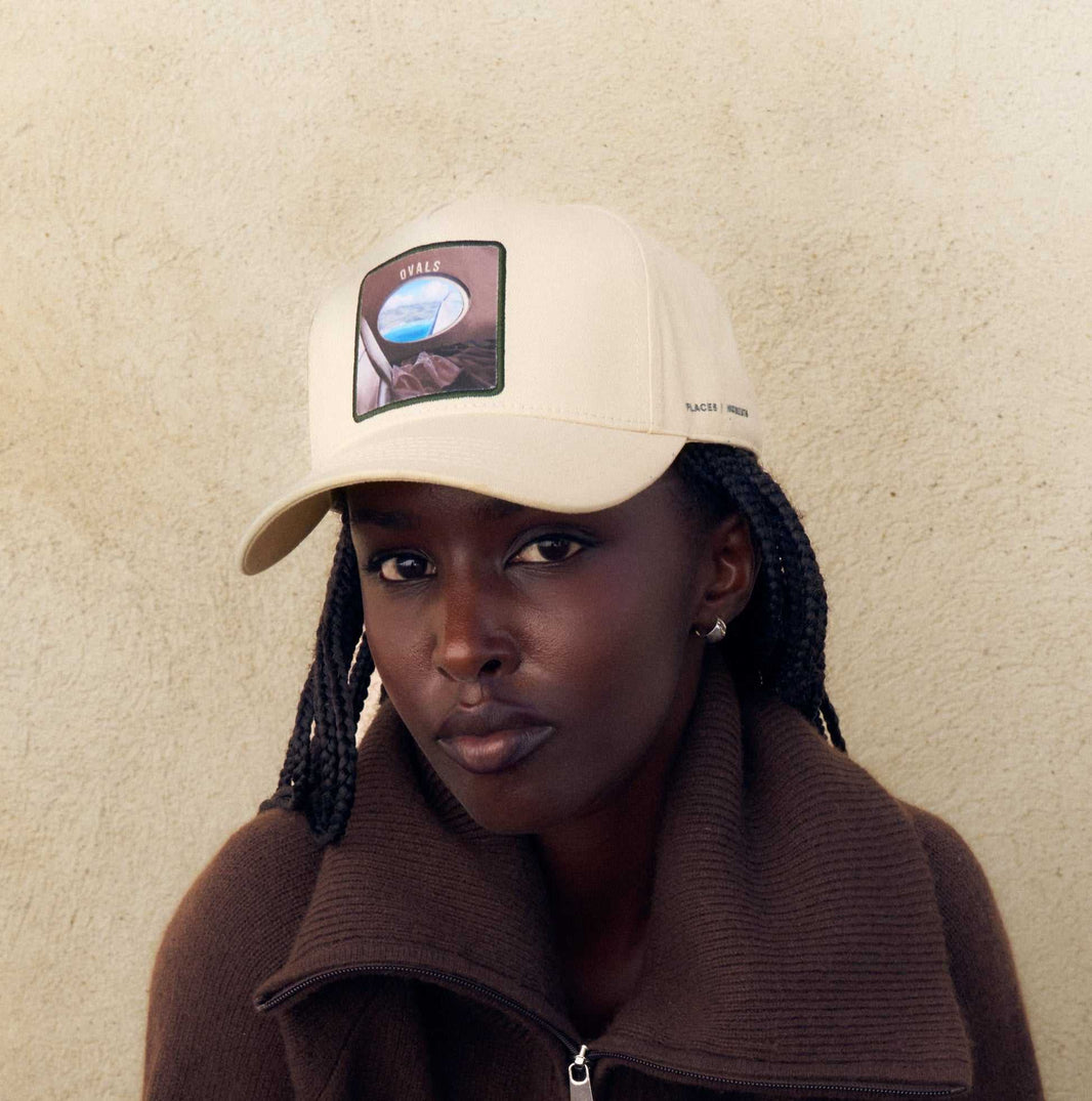 The Ovals baseball cap in Isla Crema off-white cotton, with the oval airplane window patch on the front in Forte Green.