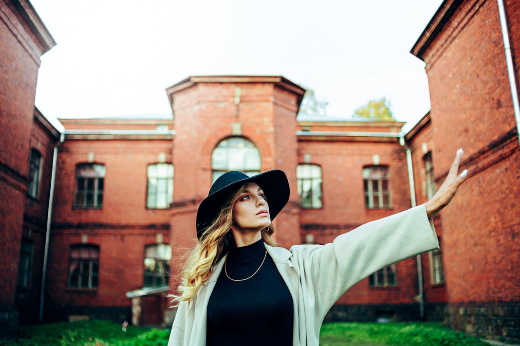 woman in white long sleeve shirt and black hat standing near brown concrete building during daytime