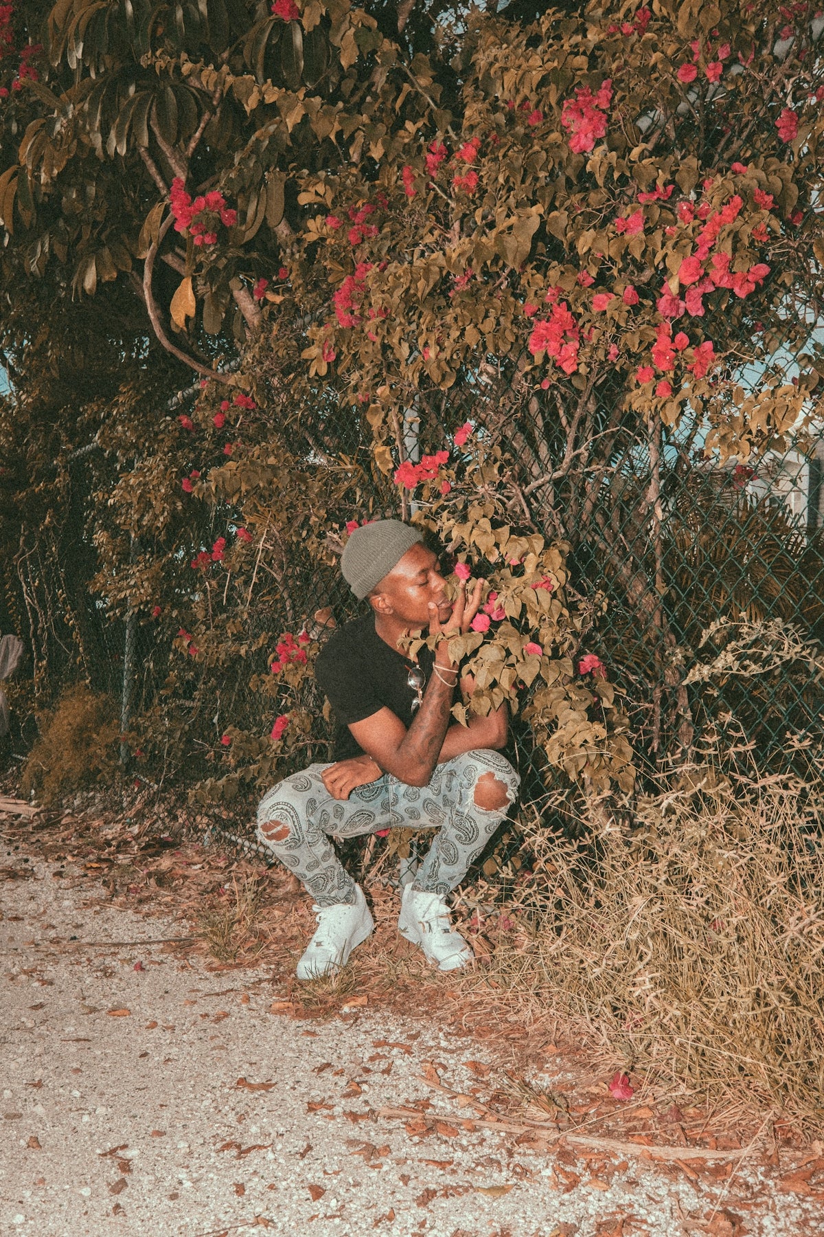 man in brown and white t-shirt and gray pants sitting on brown dried leaves during