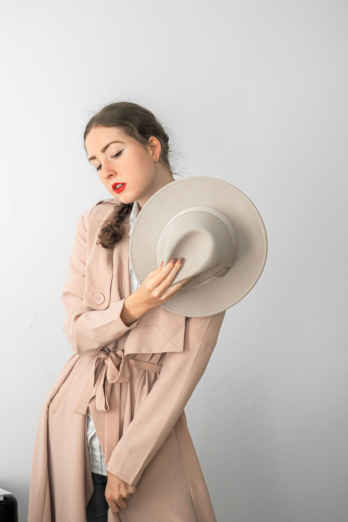 a woman in a trench coat holding a hat