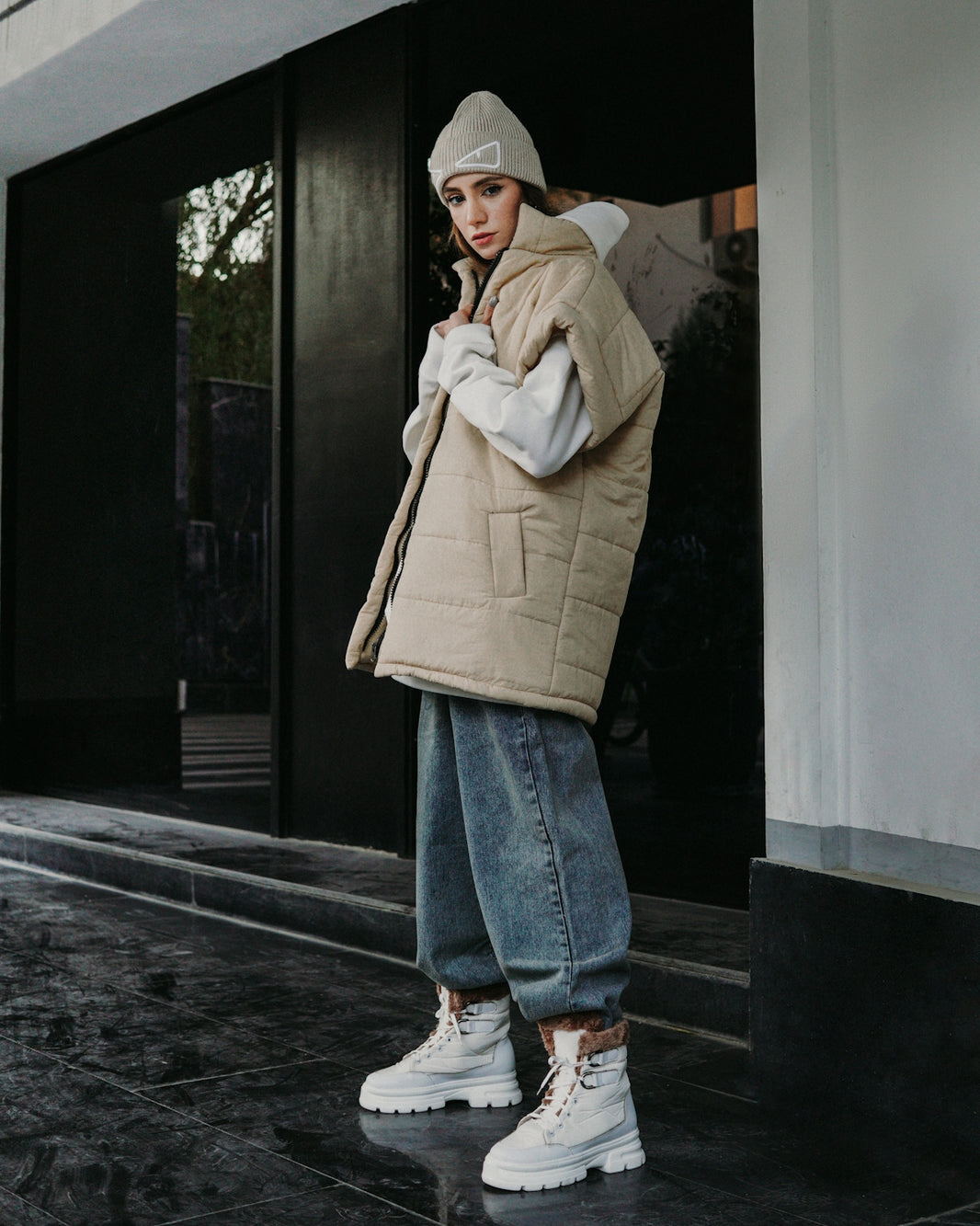 a woman standing on a sidewalk wearing a jacket and jeans