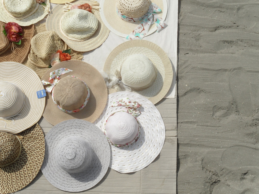 a table topped with lots of hats on top of a beach