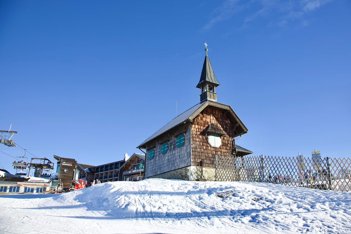 a small wooden church with a steeple on top of a snowy hill