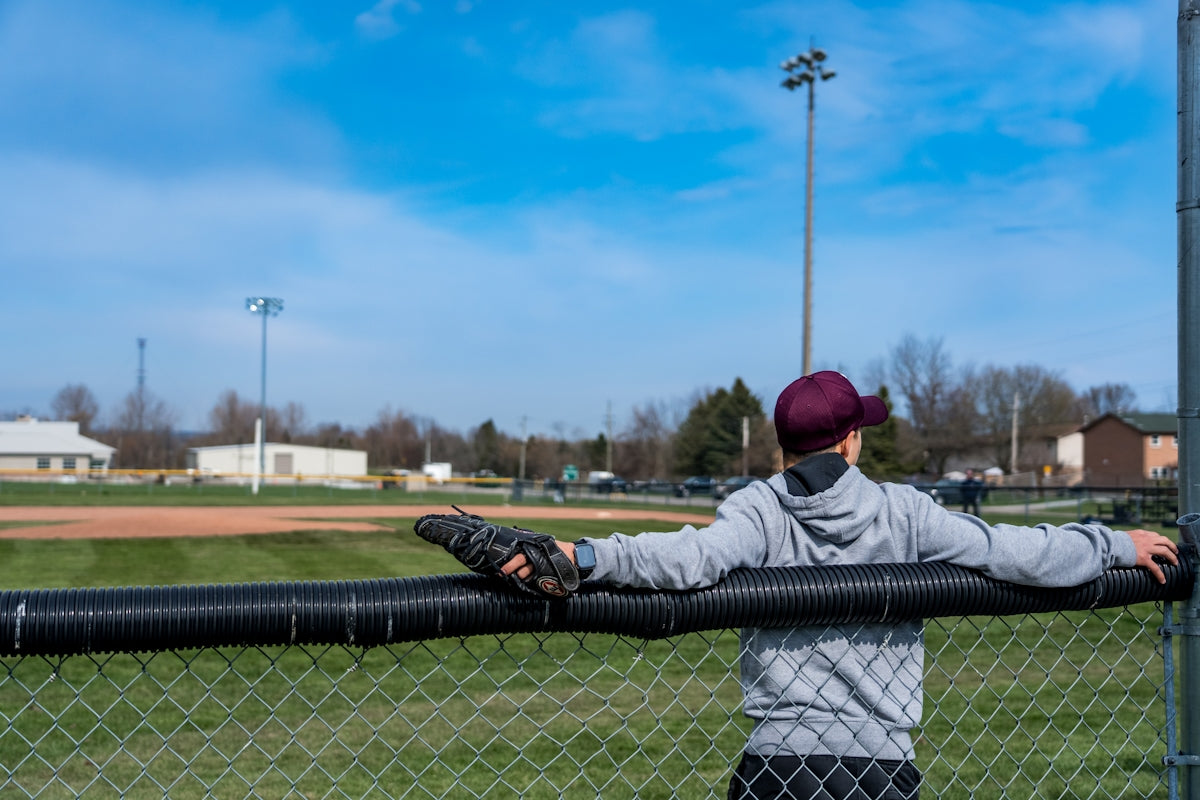 a young boy leaning on a fence at a baseball field