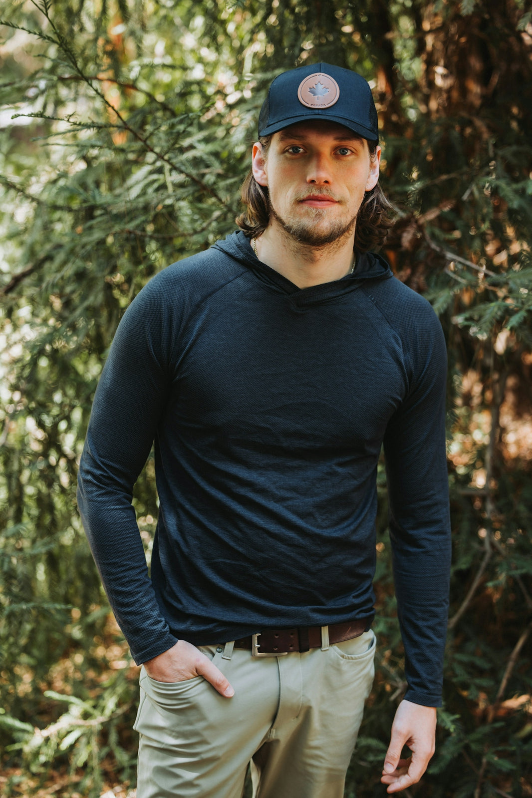 A man standing in front of trees wearing a hat