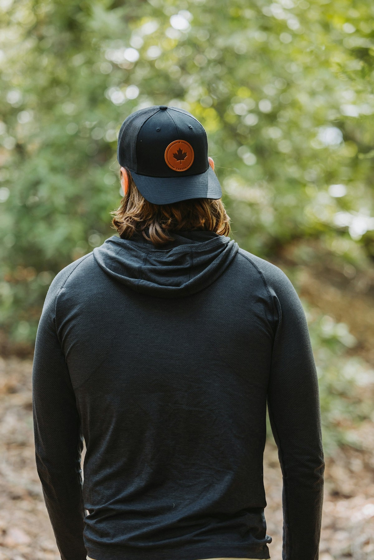 A man in a black hoodie and a hat walking in the woods