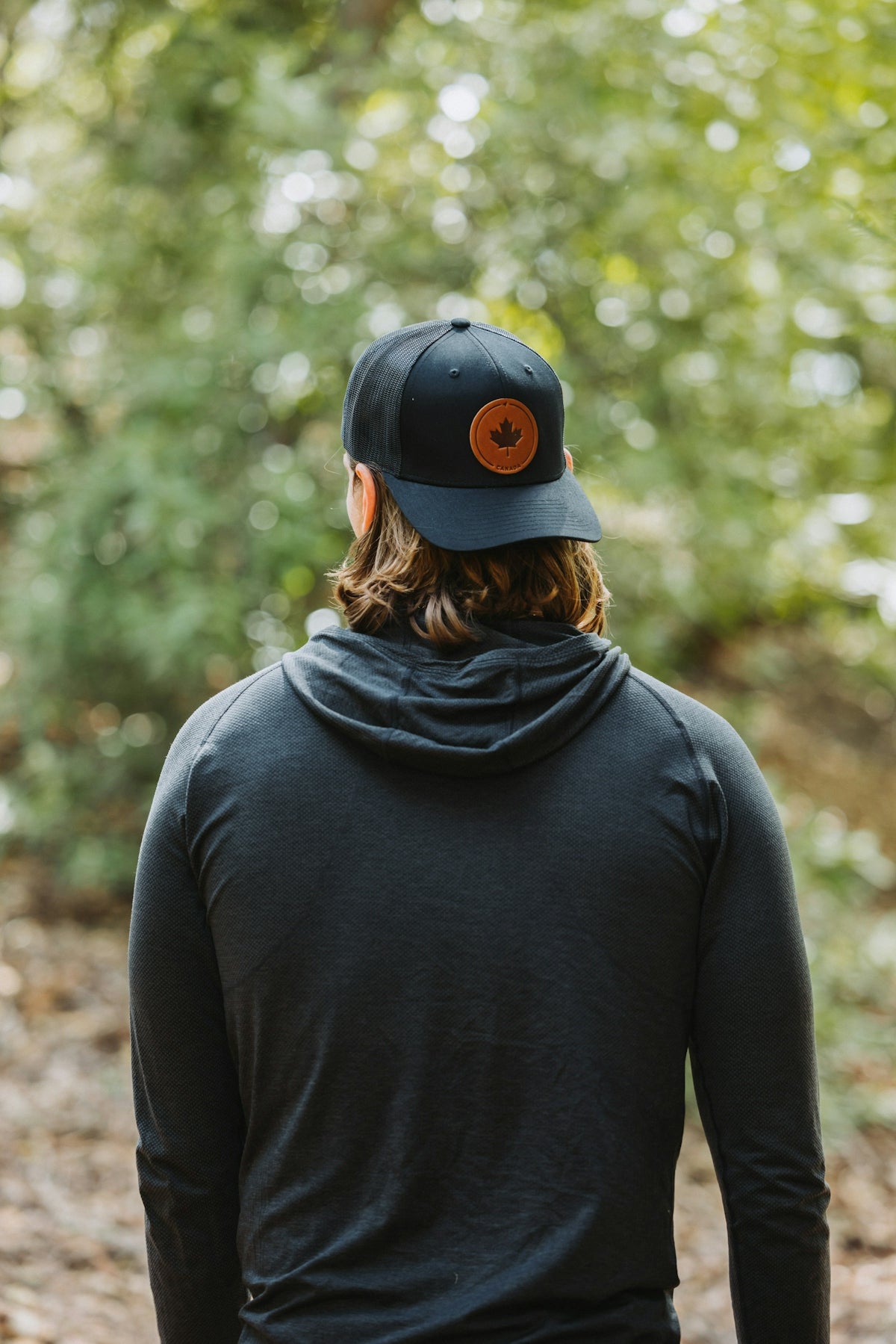 A man in a black hoodie and a hat walking in the woods