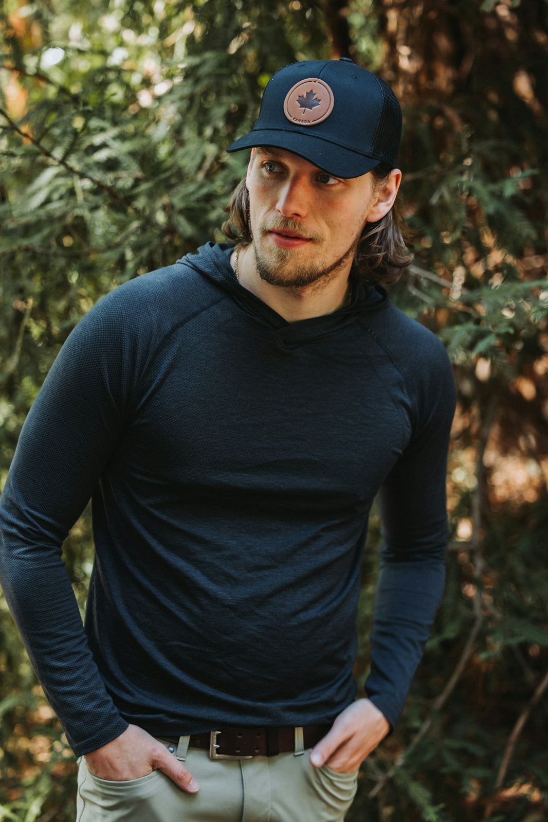 A man standing in front of trees wearing a hat