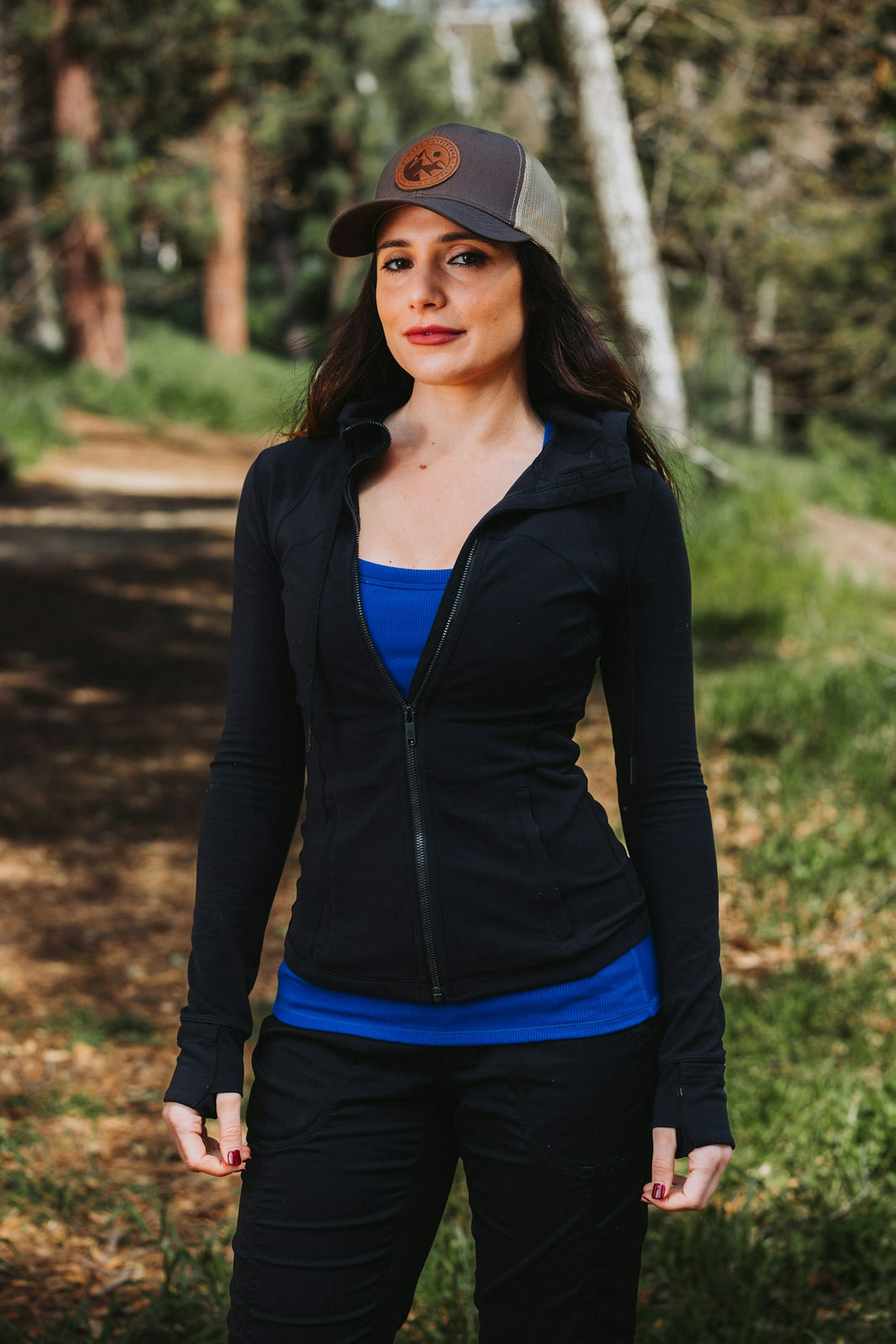 A woman standing in the woods wearing a hat