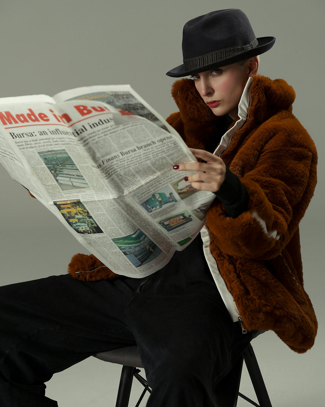 A woman sitting on a stool reading a newspaper