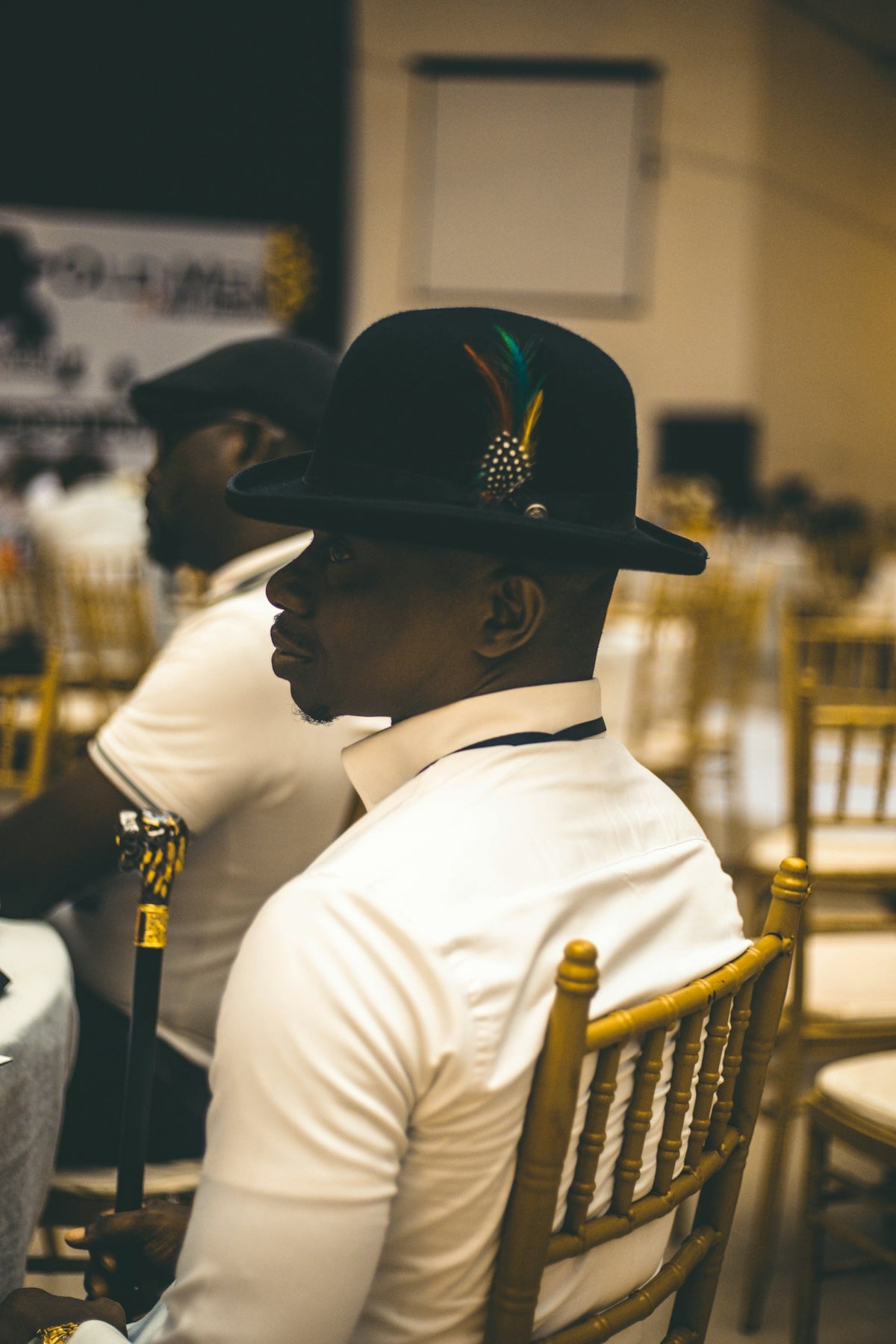 A man wearing a hat with feathers is seated.