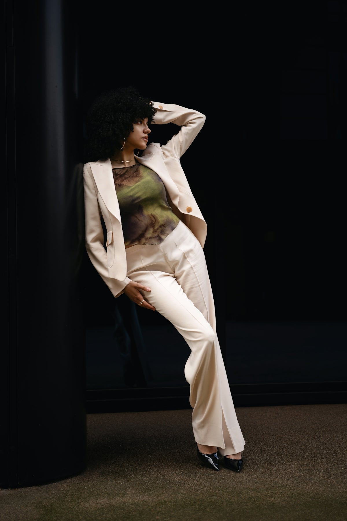 A woman poses in a suit against a dark wall.