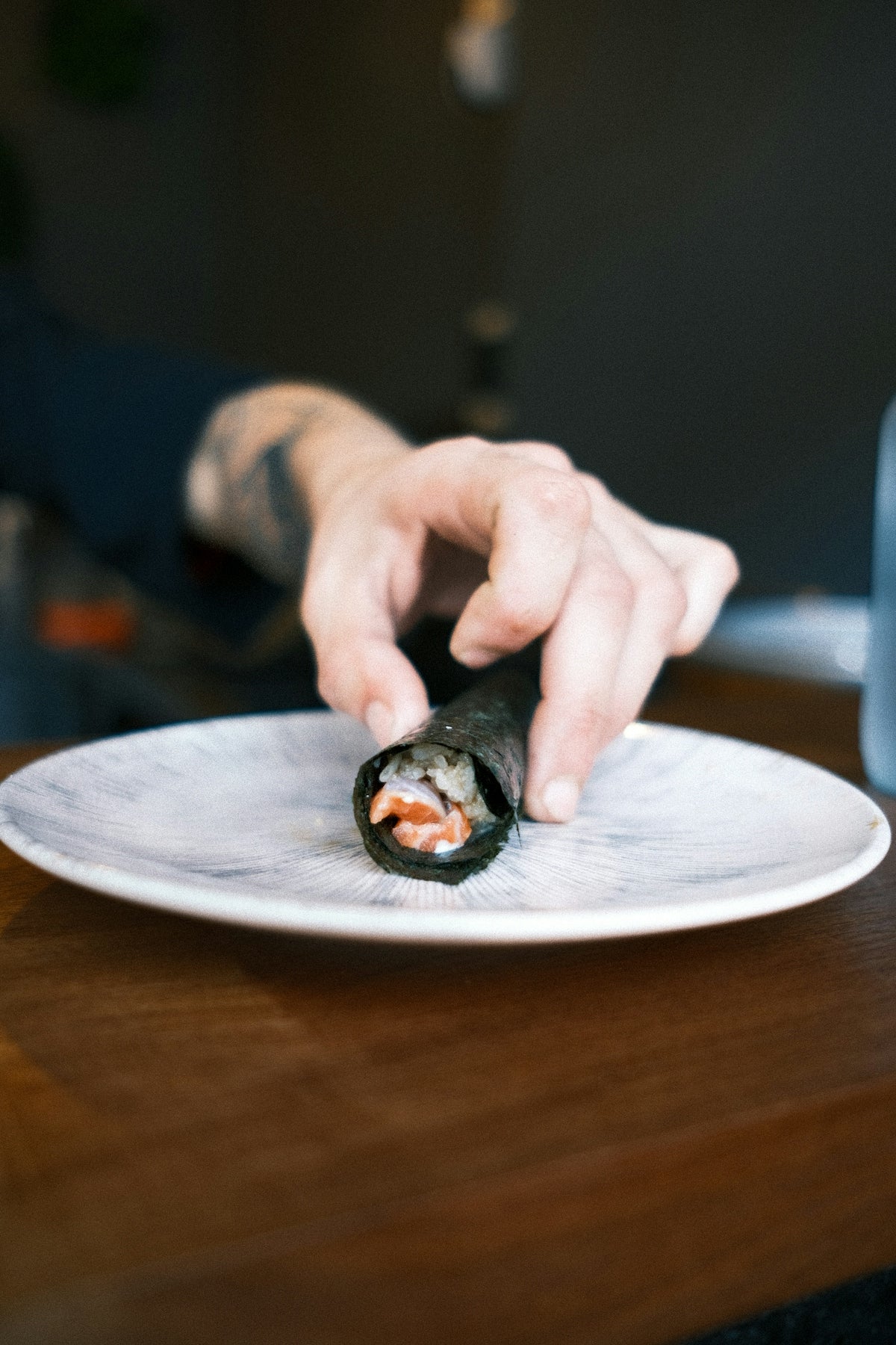 Hand places a sushi hand roll on a plate.