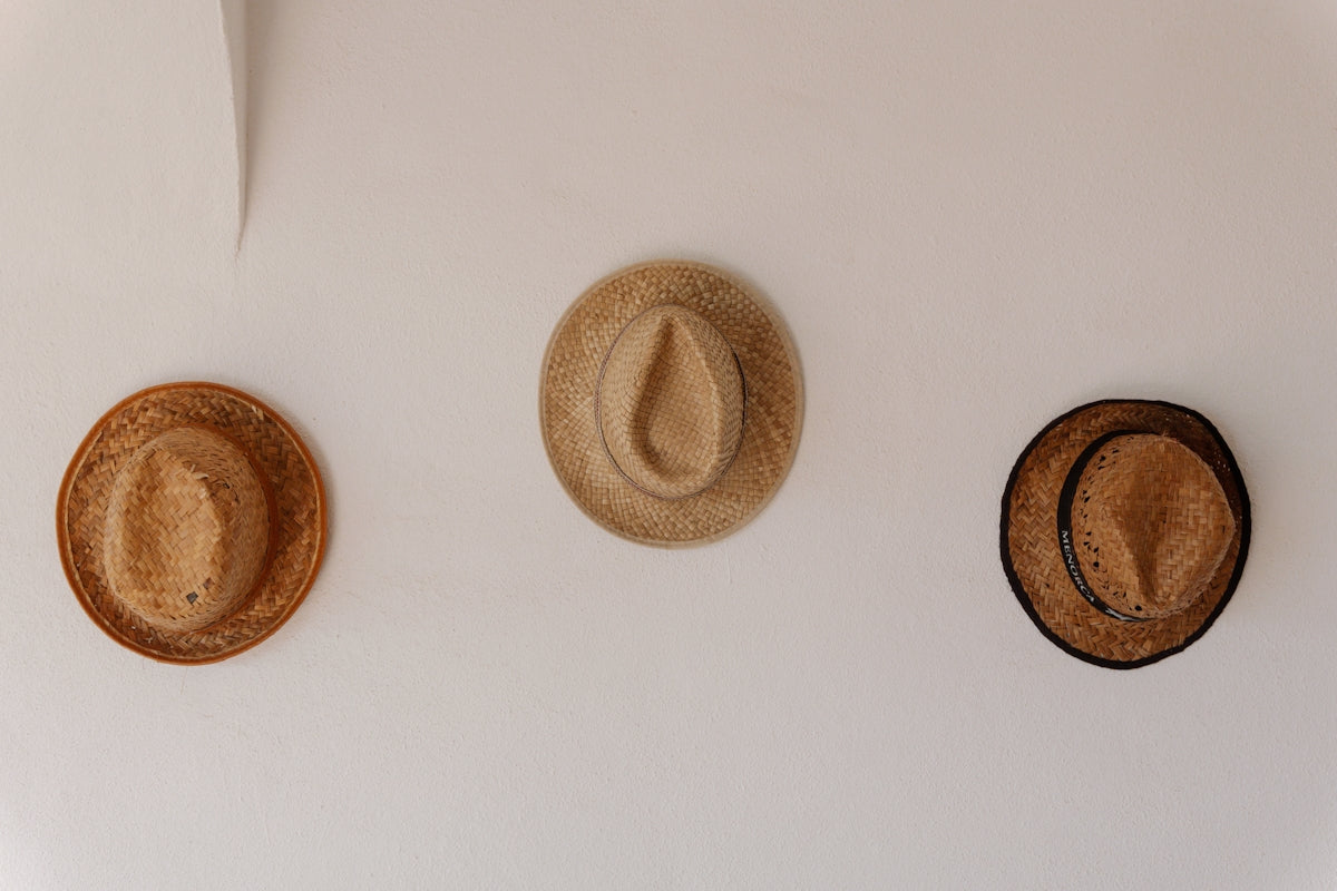 Three straw hats hang on a white wall.