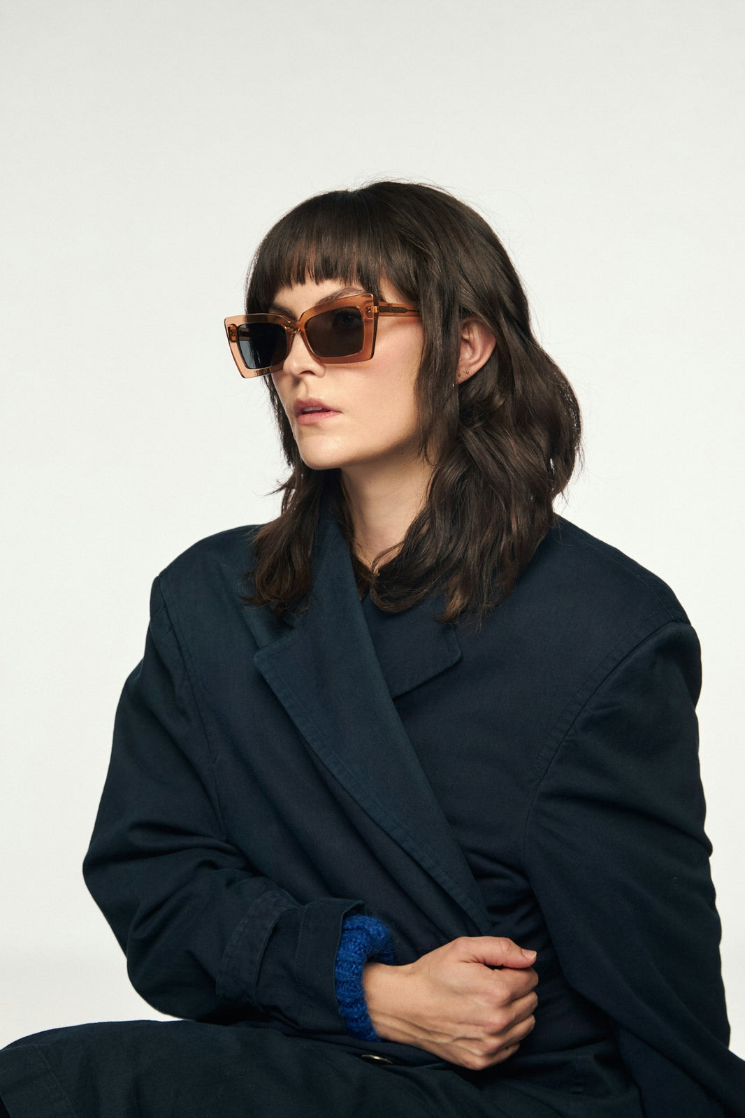 Woman models sunglasses, wearing a coat.