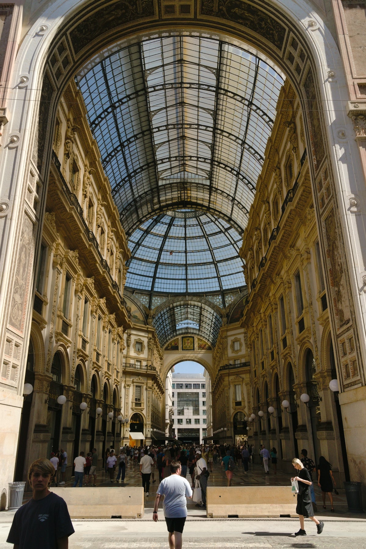 People walking through a grand, ornate glass-covered arcade.