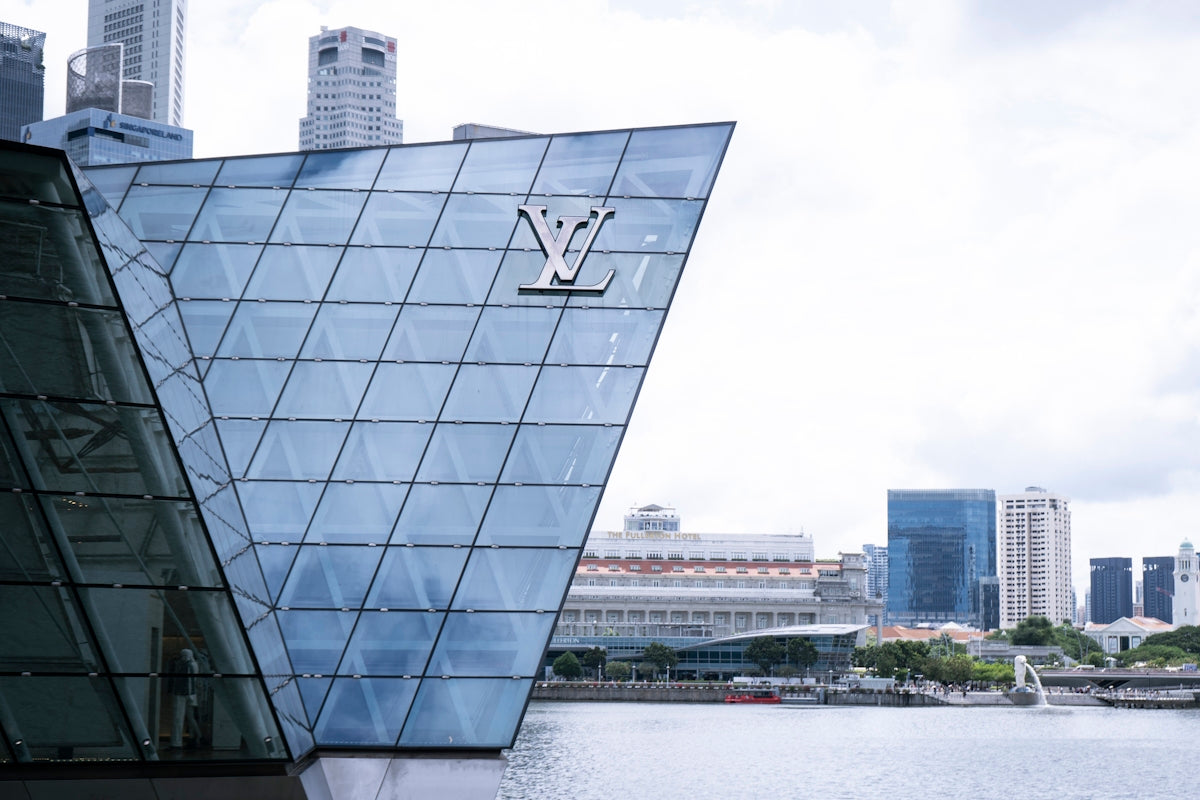 Modern glass building with louis vuitton logo by water.