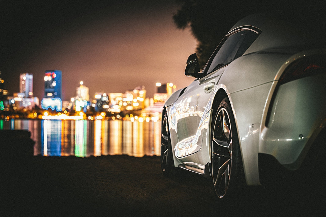 White sports car parked by a city skyline at night