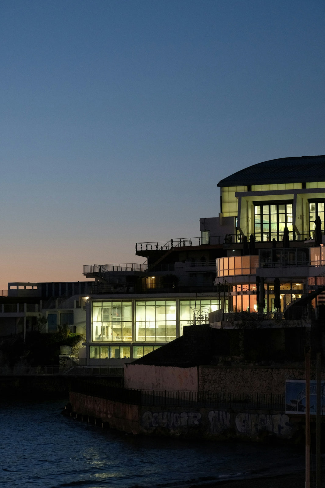 Modern buildings illuminated at dusk by the water.