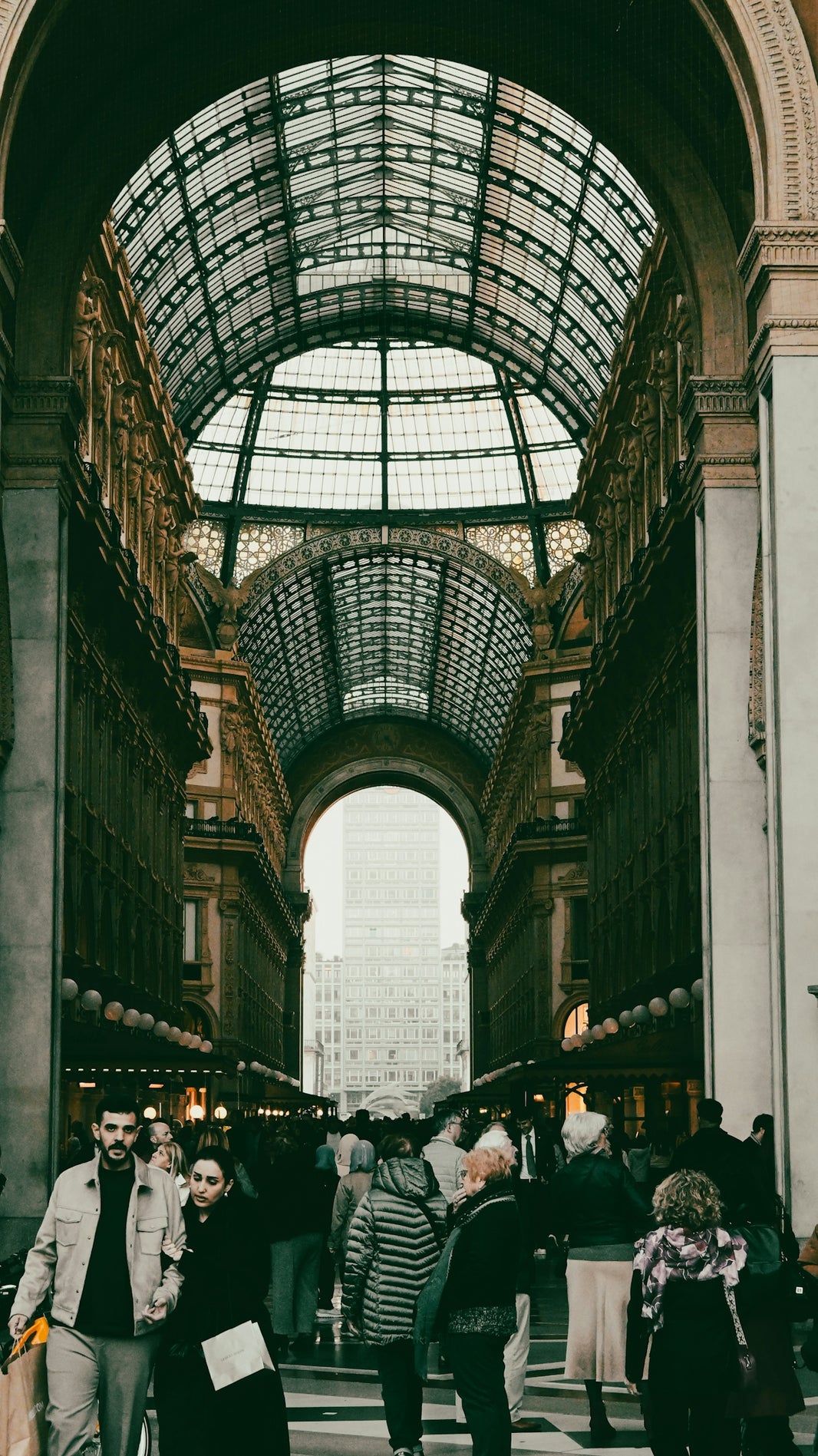People walking through a grand arched building with glass ceiling.
