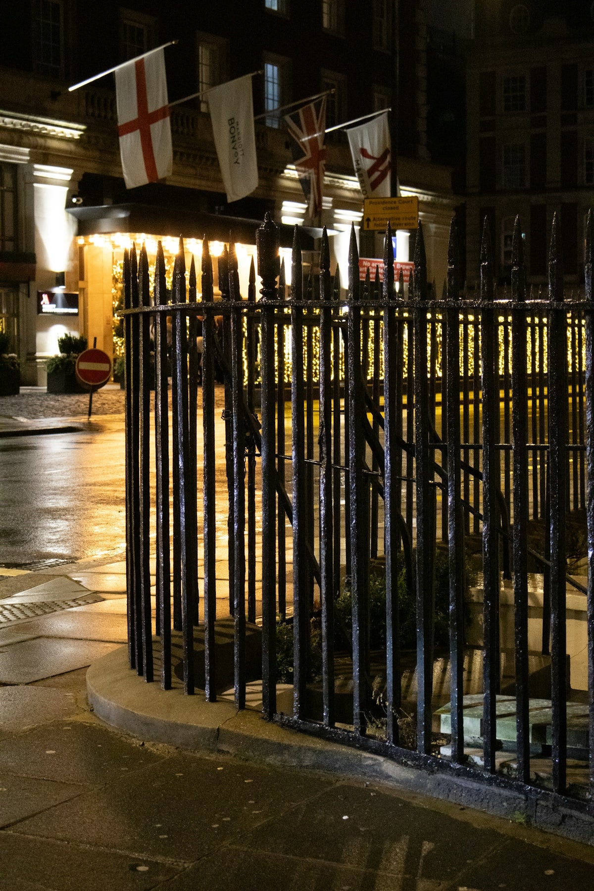 Ornate fence in front of illuminated building with flags