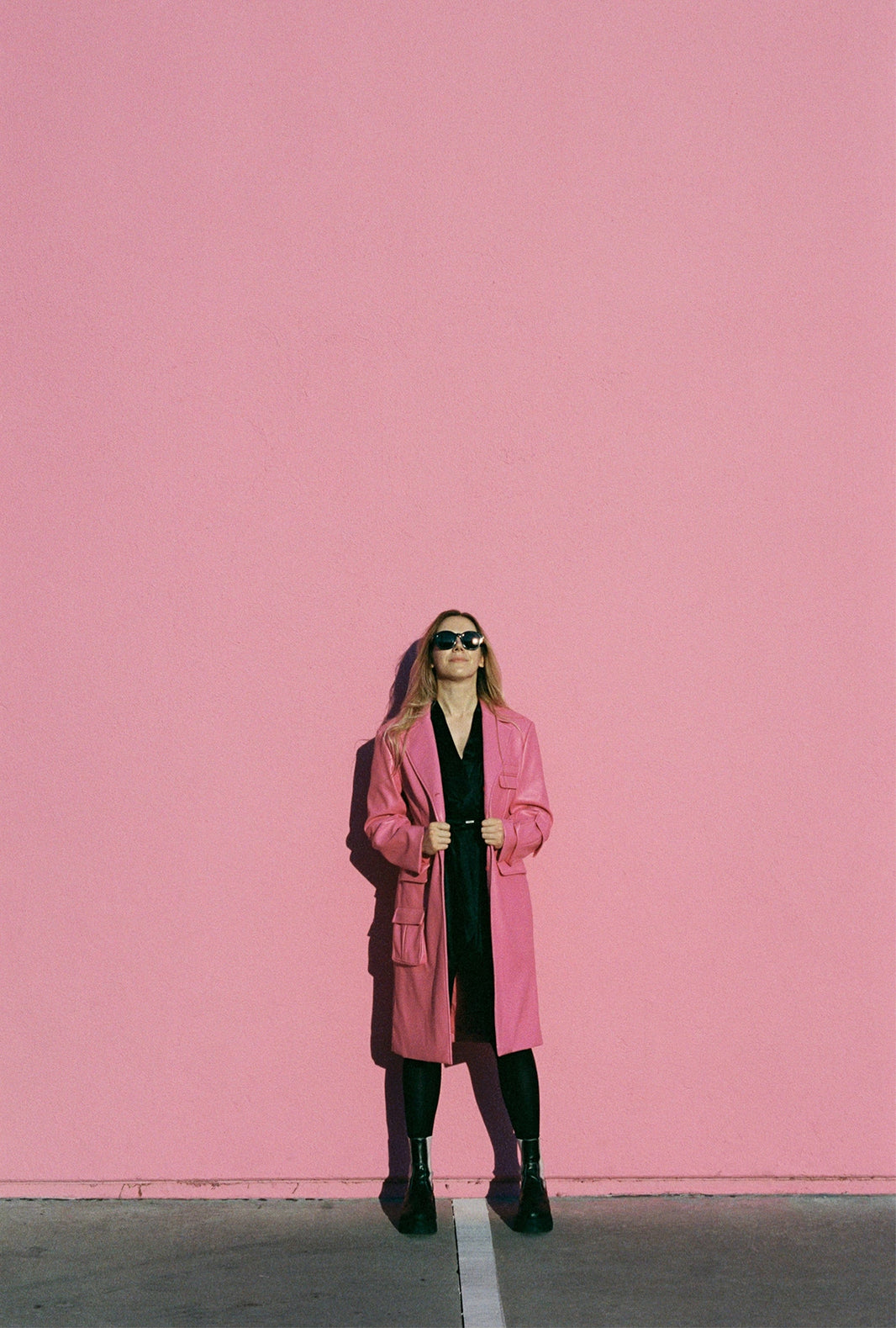 Woman in pink coat stands against pink wall