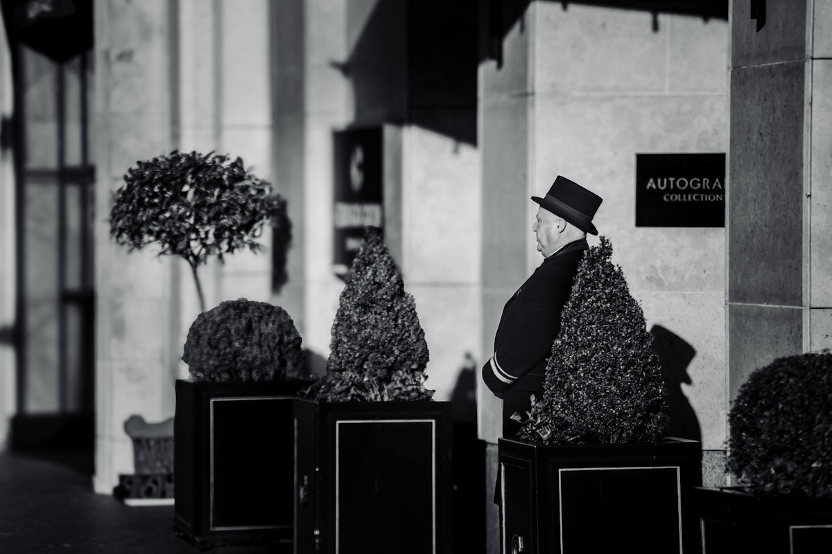 Man in top hat walks past potted trees