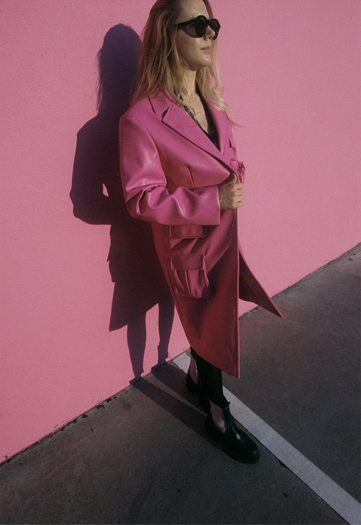 Woman in pink coat stands against pink wall