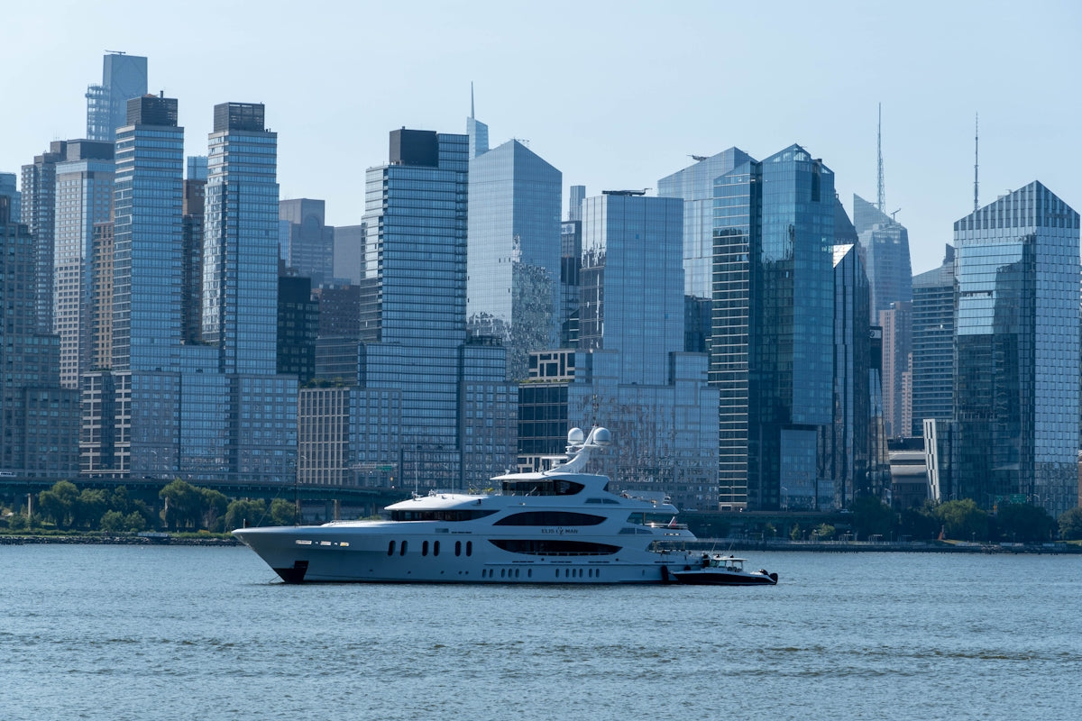 Large white yacht sails on water with city skyline.
