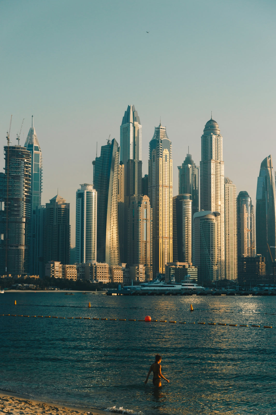 A person walks into the ocean with skyscrapers behind.