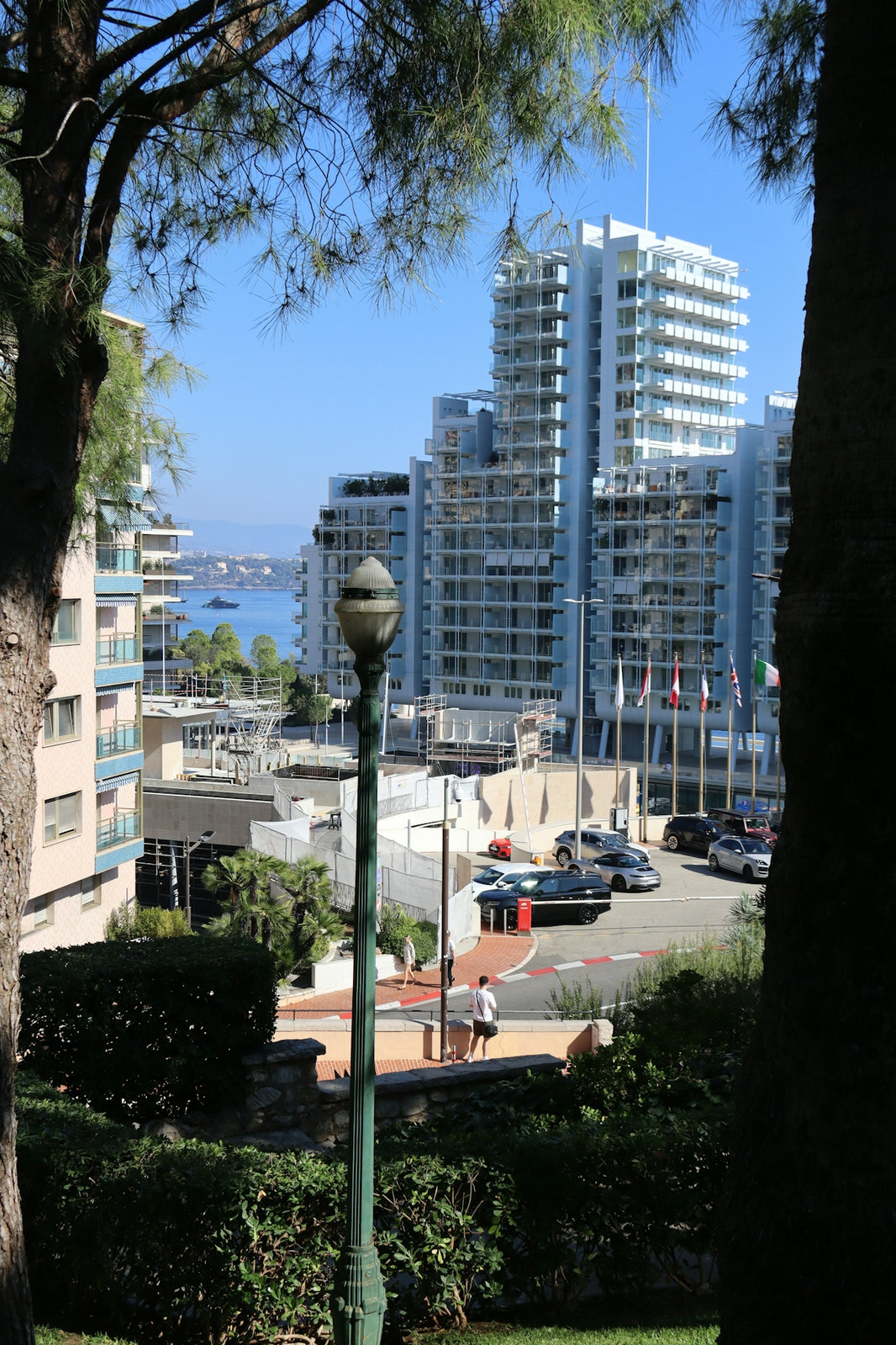 Modern buildings overlook a street with cars and the ocean.