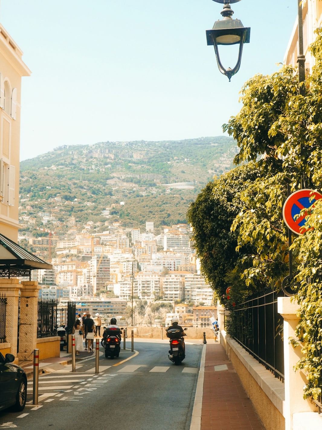 Two scooters ride down a sunny street in monaco.