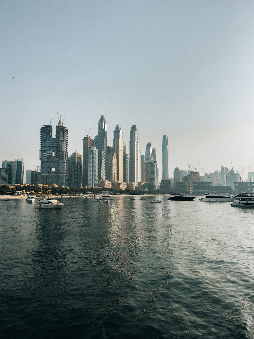 Modern skyscrapers rise above a calm bay with boats.