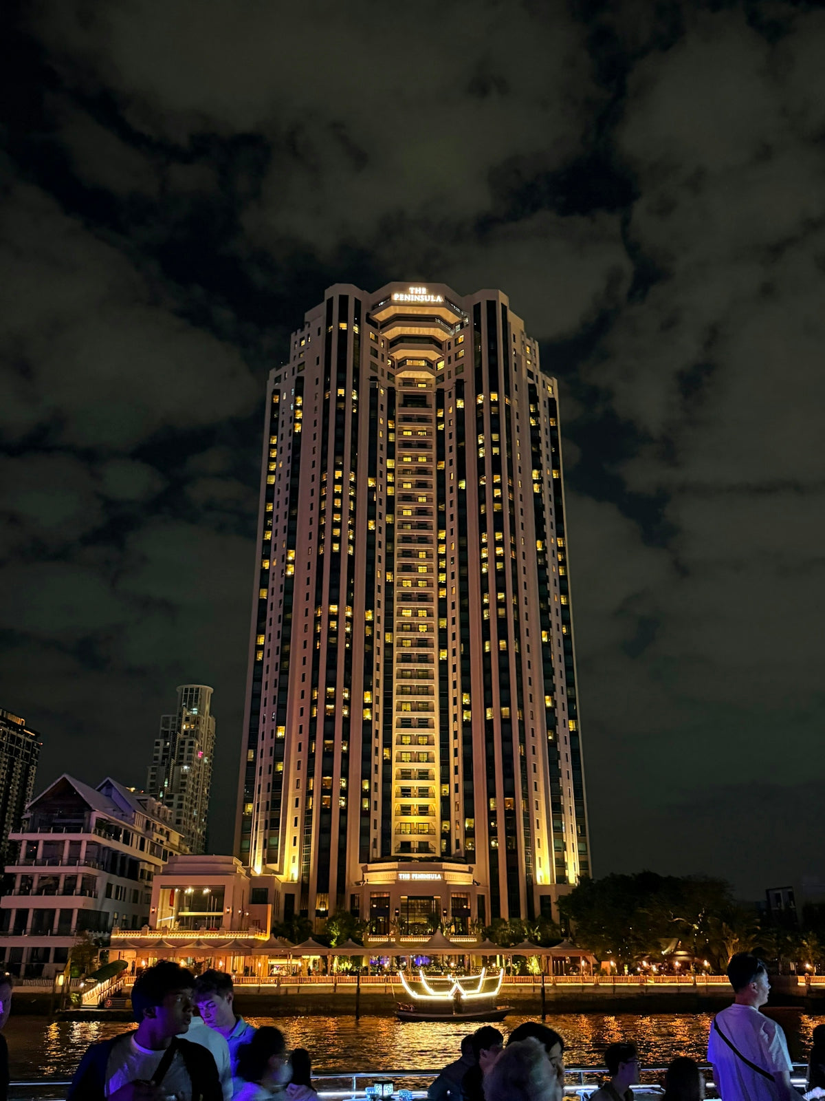 Tall illuminated skyscraper at night with clouds above
