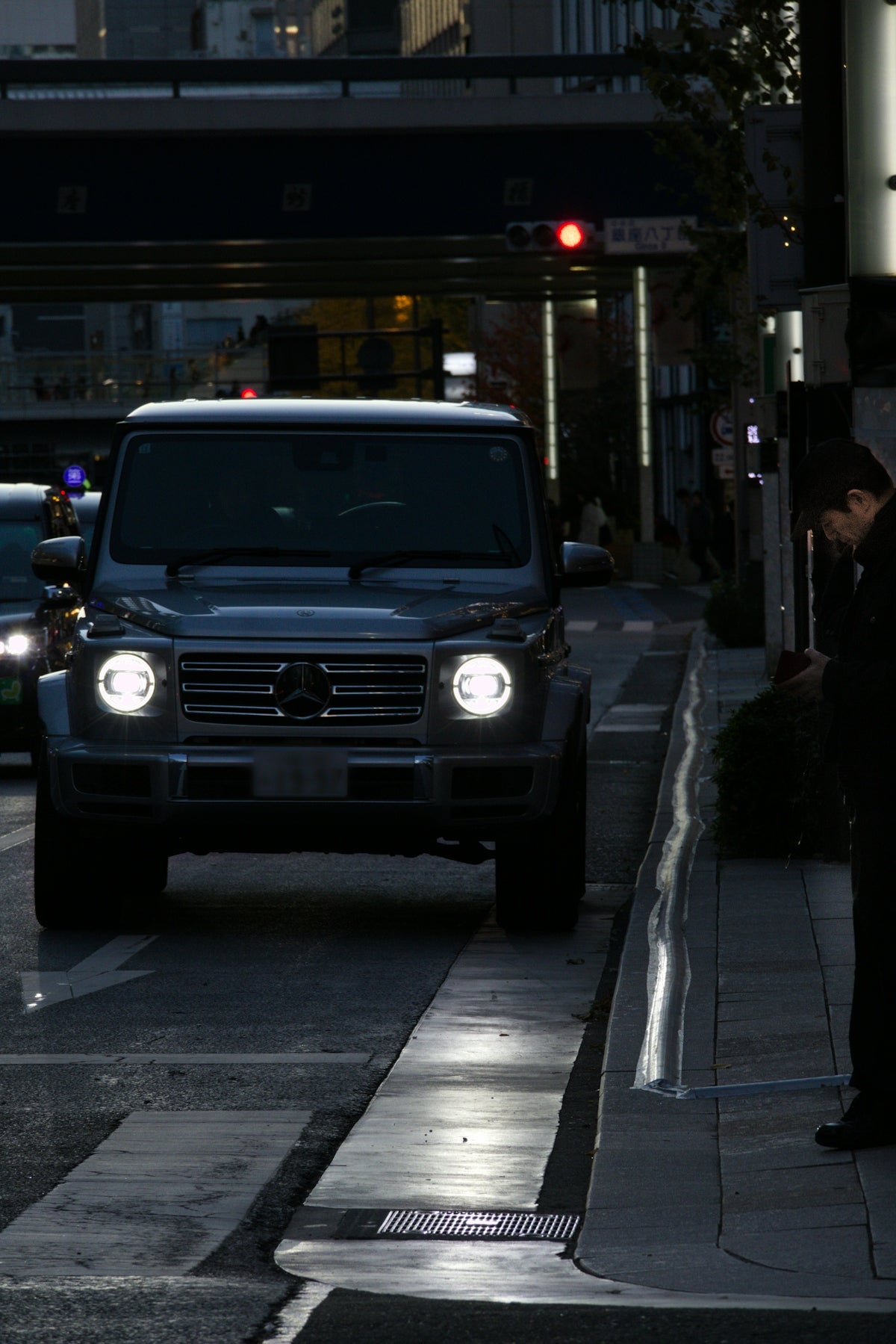 A dark mercedes g-wagon drives down a city street.