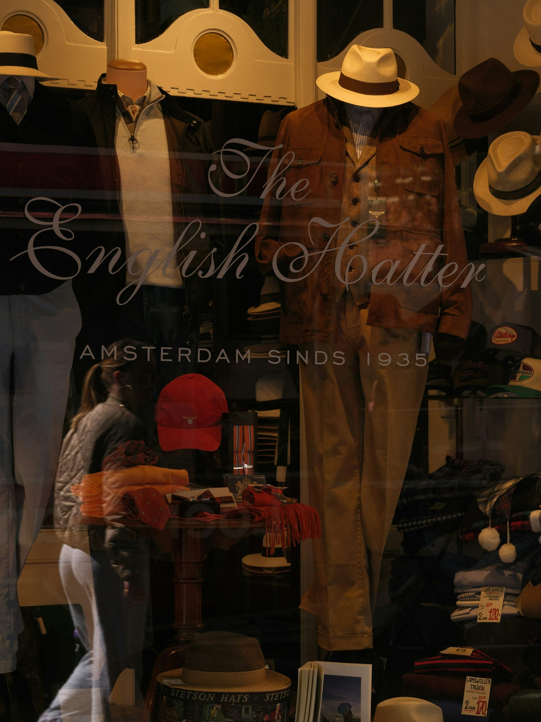 Mannequins display hats and clothing in a shop window.