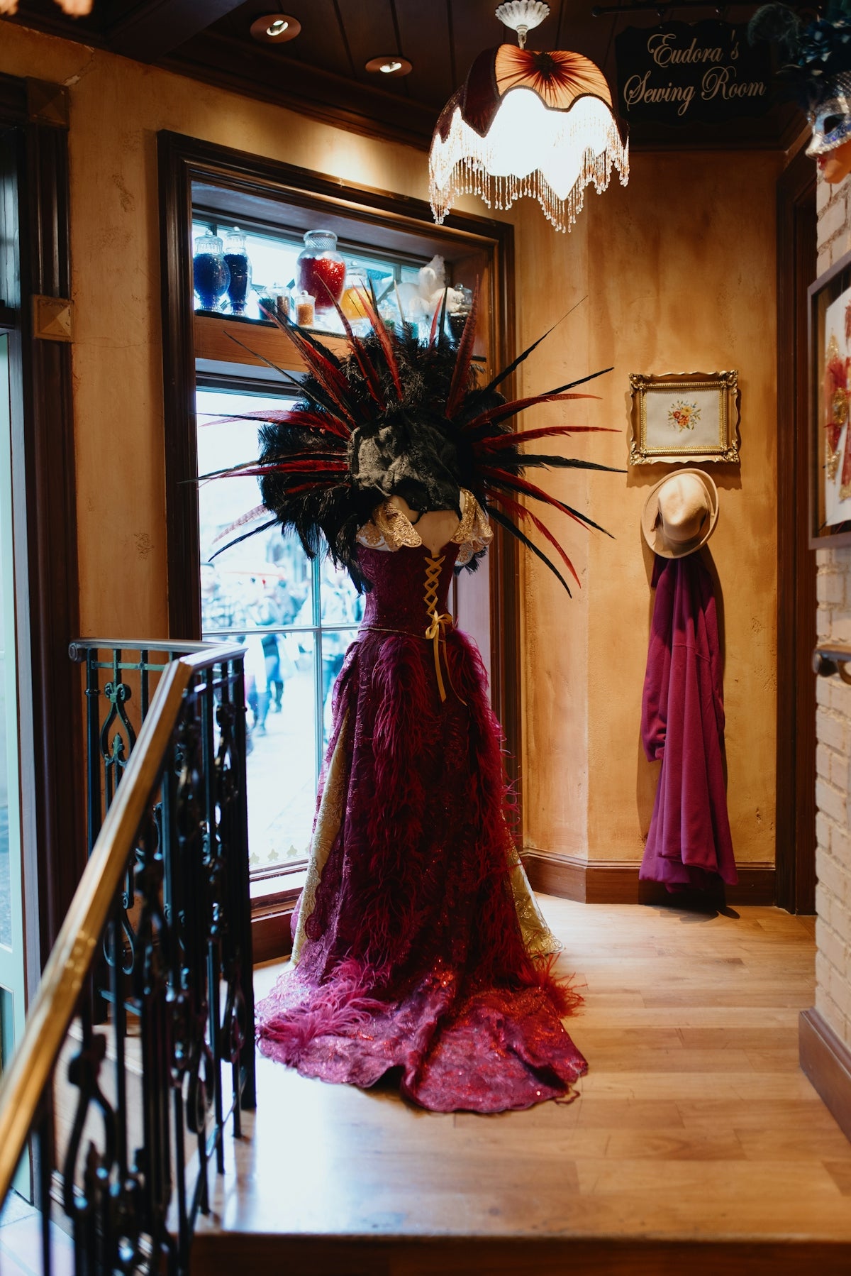 Mannequin wearing an ornate dark red feathered dress indoors.