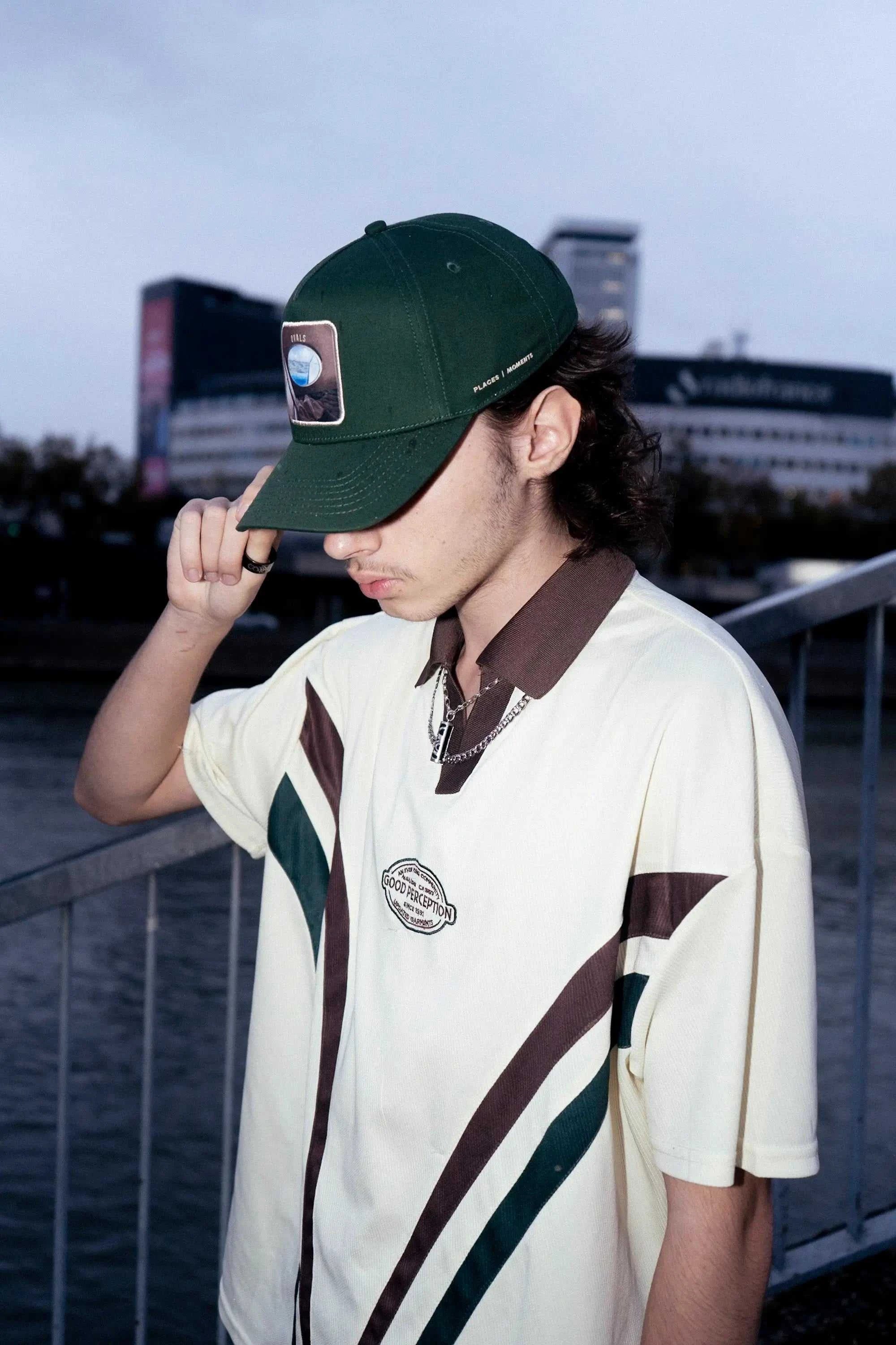 Man wearing dark green Ovals Baseball Cap with embroidered patch and casual sporty shirt outdoors