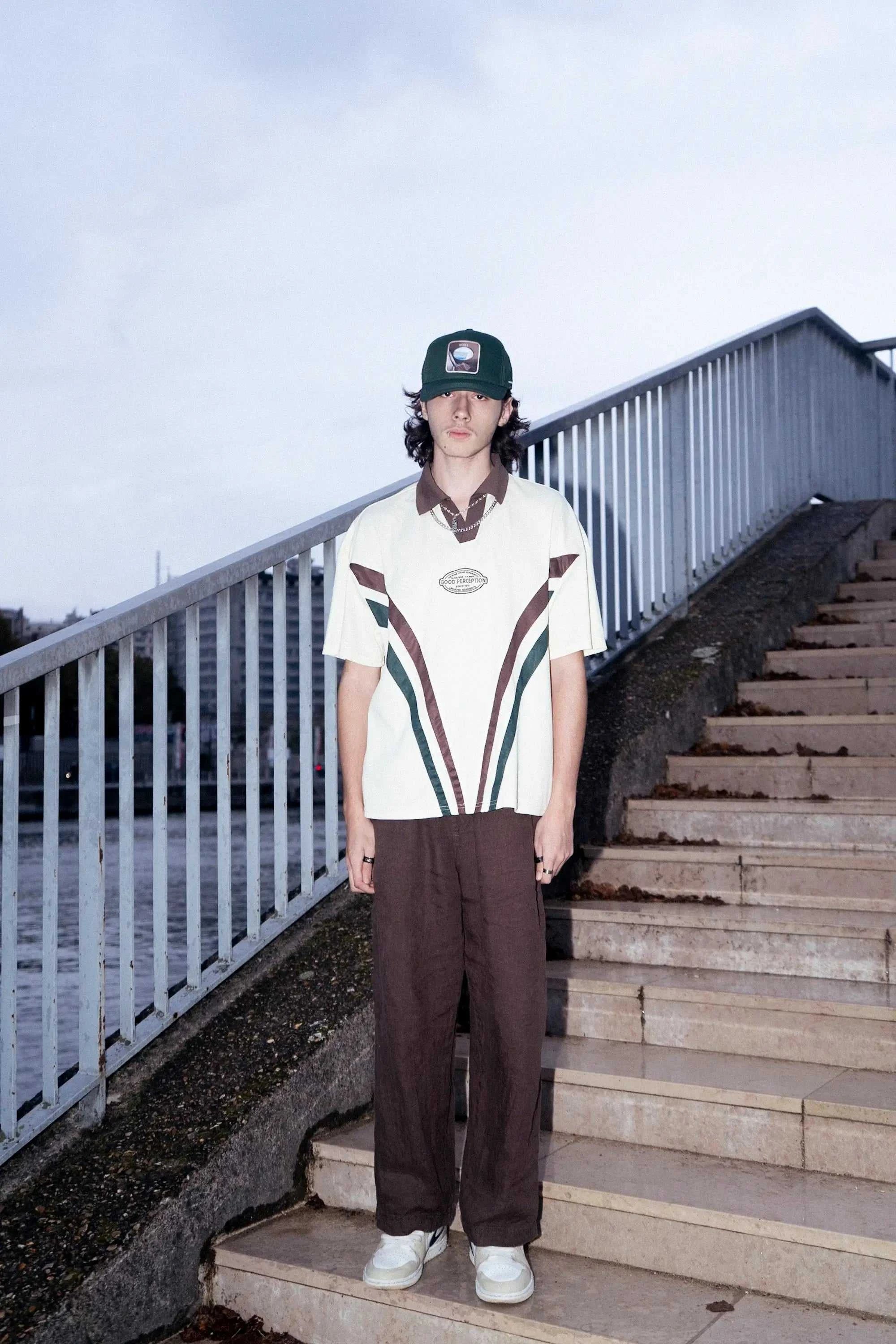 Man wearing deep forest green Ovals Baseball Cap with embroidered patch, styled with casual vintage outfit outdoors on stairs