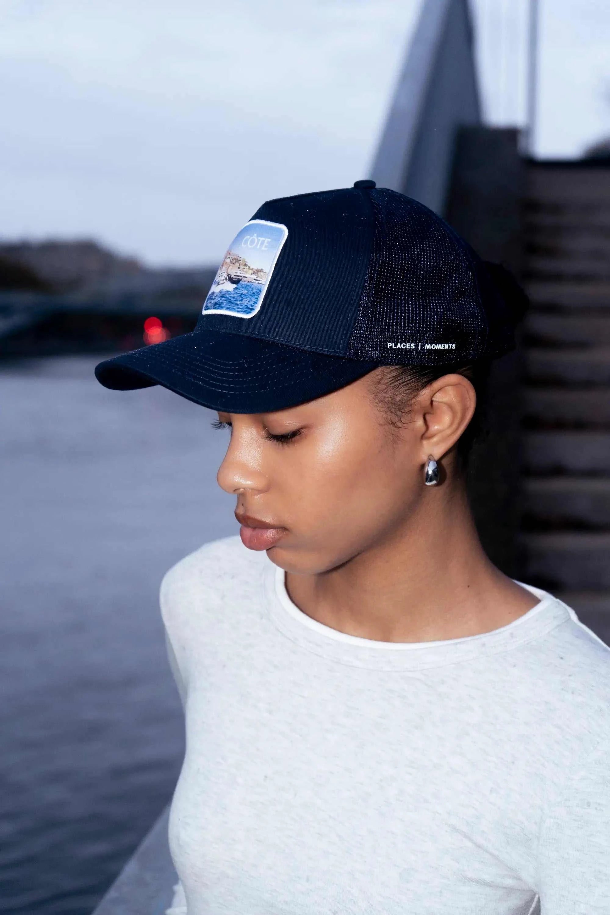 Côte Mesh-Back Trucker Hat in Indie Blue with structured front, mesh back, curved brim, and Places | Moments patch worn outdoors by woman