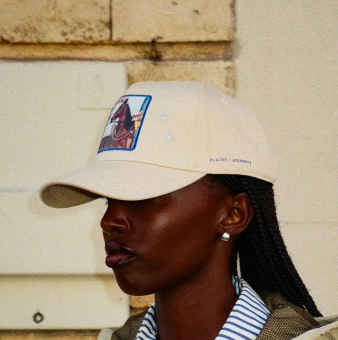 A woman in profile wearing the tan Paso Fino baseball cap, showing the horse patch, two embroidered stars and PLACES | MOMENTS over the left ear.