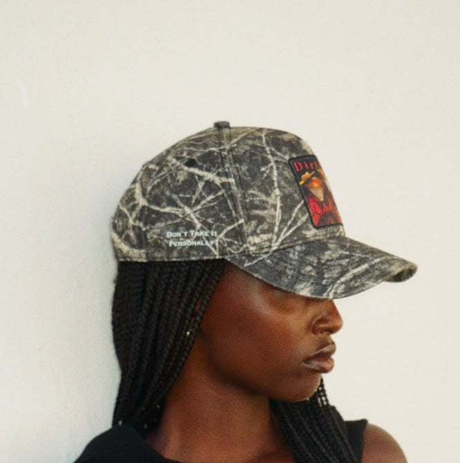 Side view of the winter branch camo Dirty Martini baseball cap, with Don't Take It Personally lettering in white down the right side.