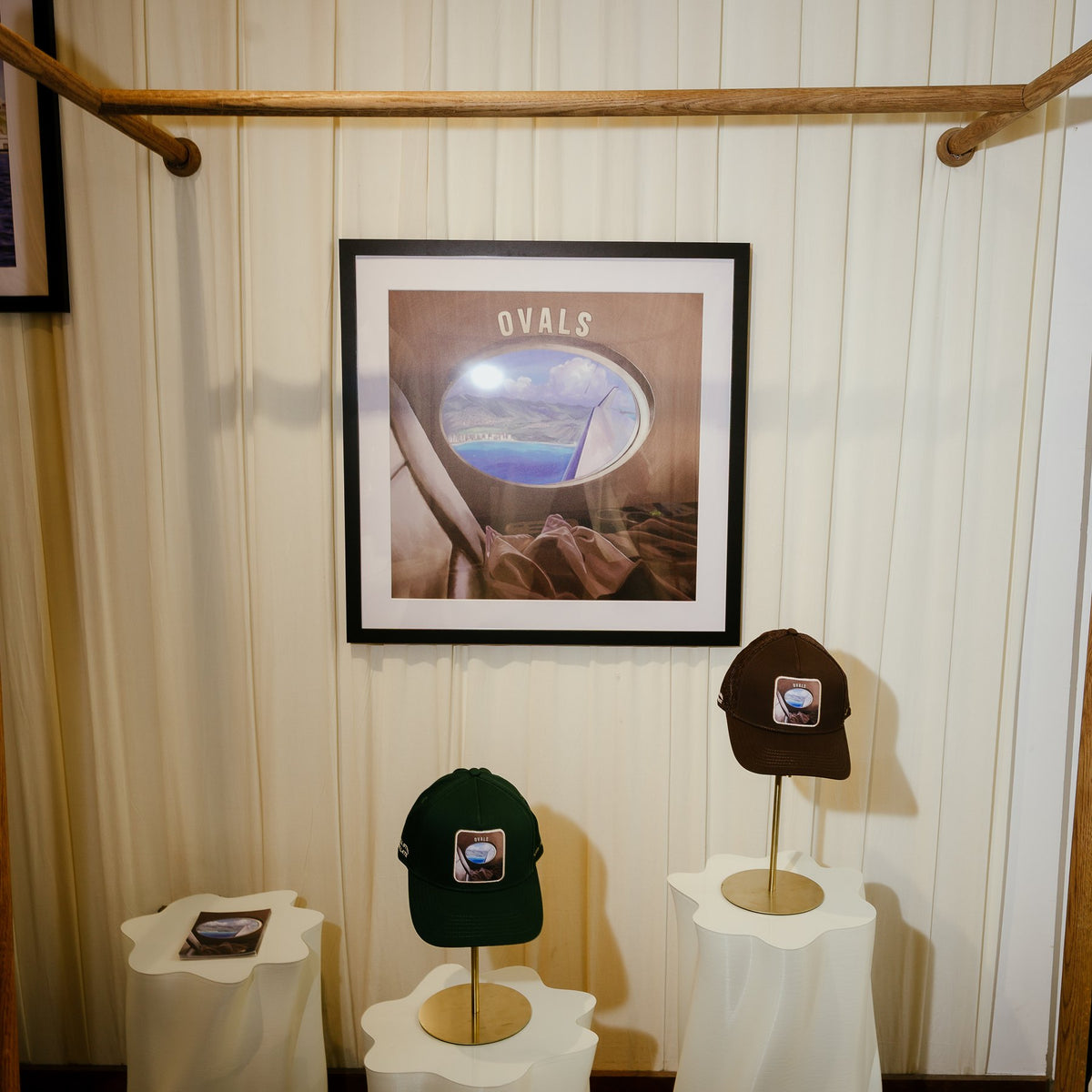 A framed print of the Ovals painting above the Ovals cap and trucker