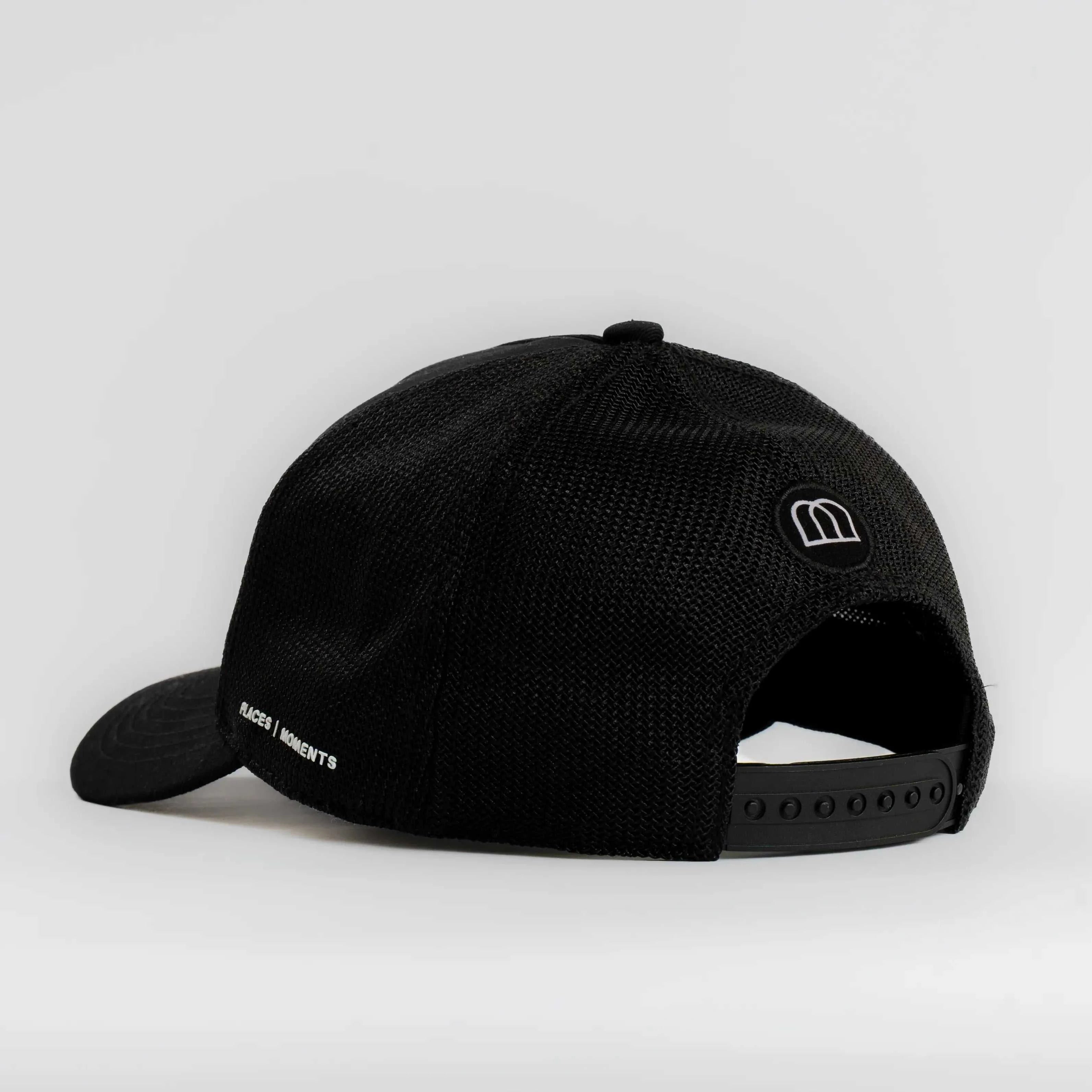 Black Nixon mesh-back trucker hat with curved brim and embroidered Places | Moments patch, breathable mesh panel, and adjustable snapback.
