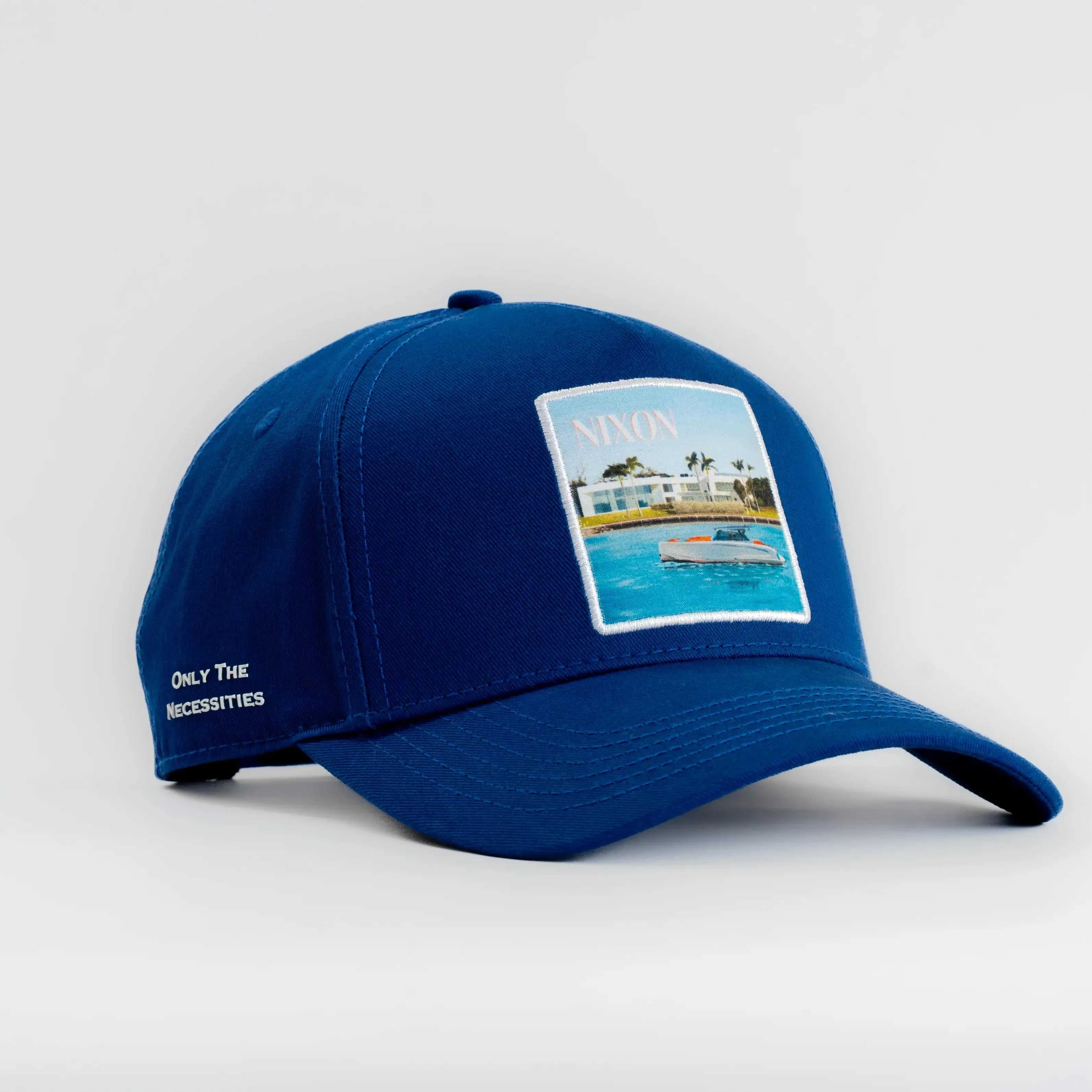 Blue Nixon Baseball Cap with structured crown and curved brim featuring coastal patch and embroidered text on side