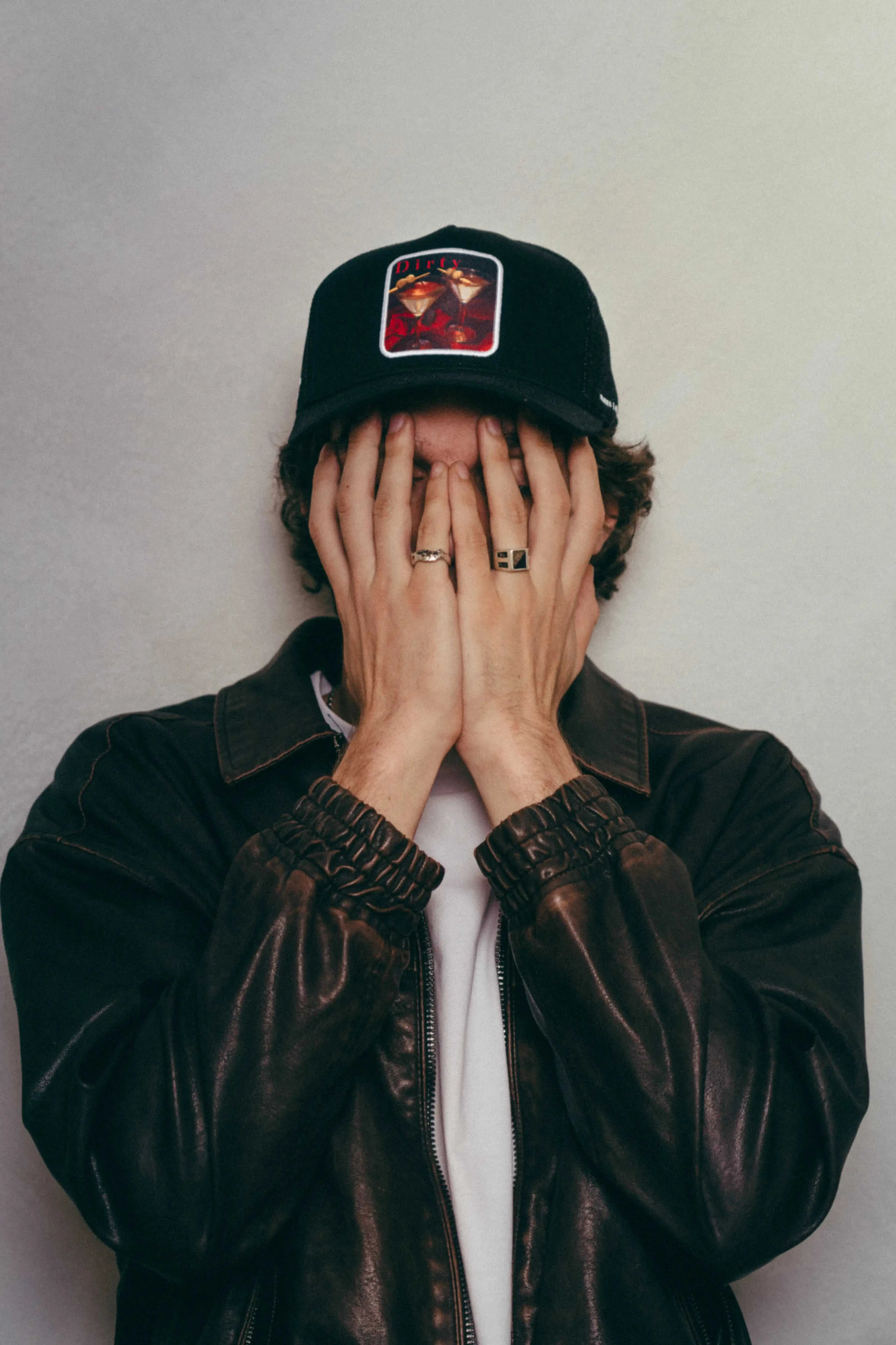 Black Dirty Martini Trucker Hat with mesh back worn by person in leather jacket covering face