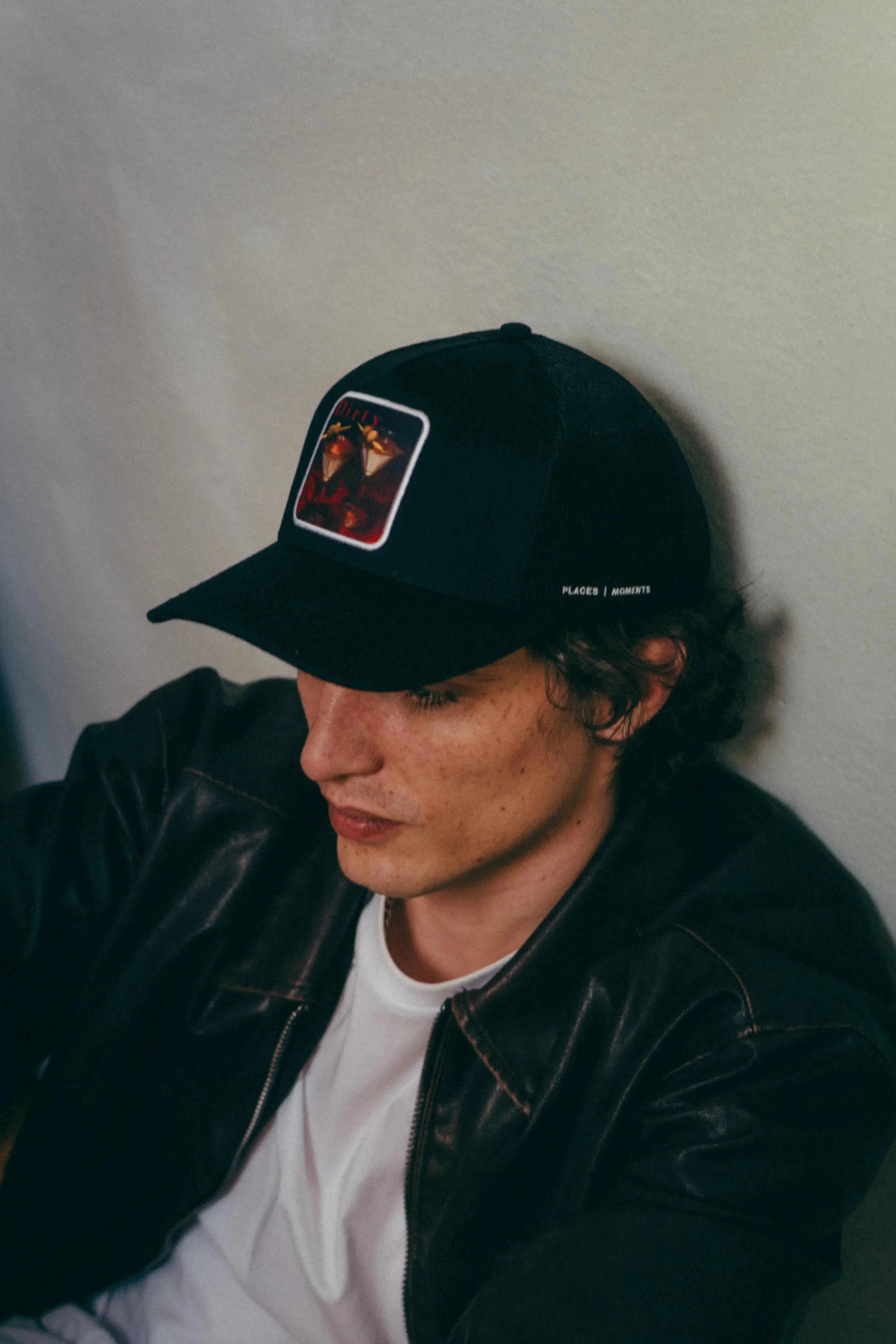 Black Dirty Martini Trucker Hat with mesh back and signature patch worn by a man in a leather jacket