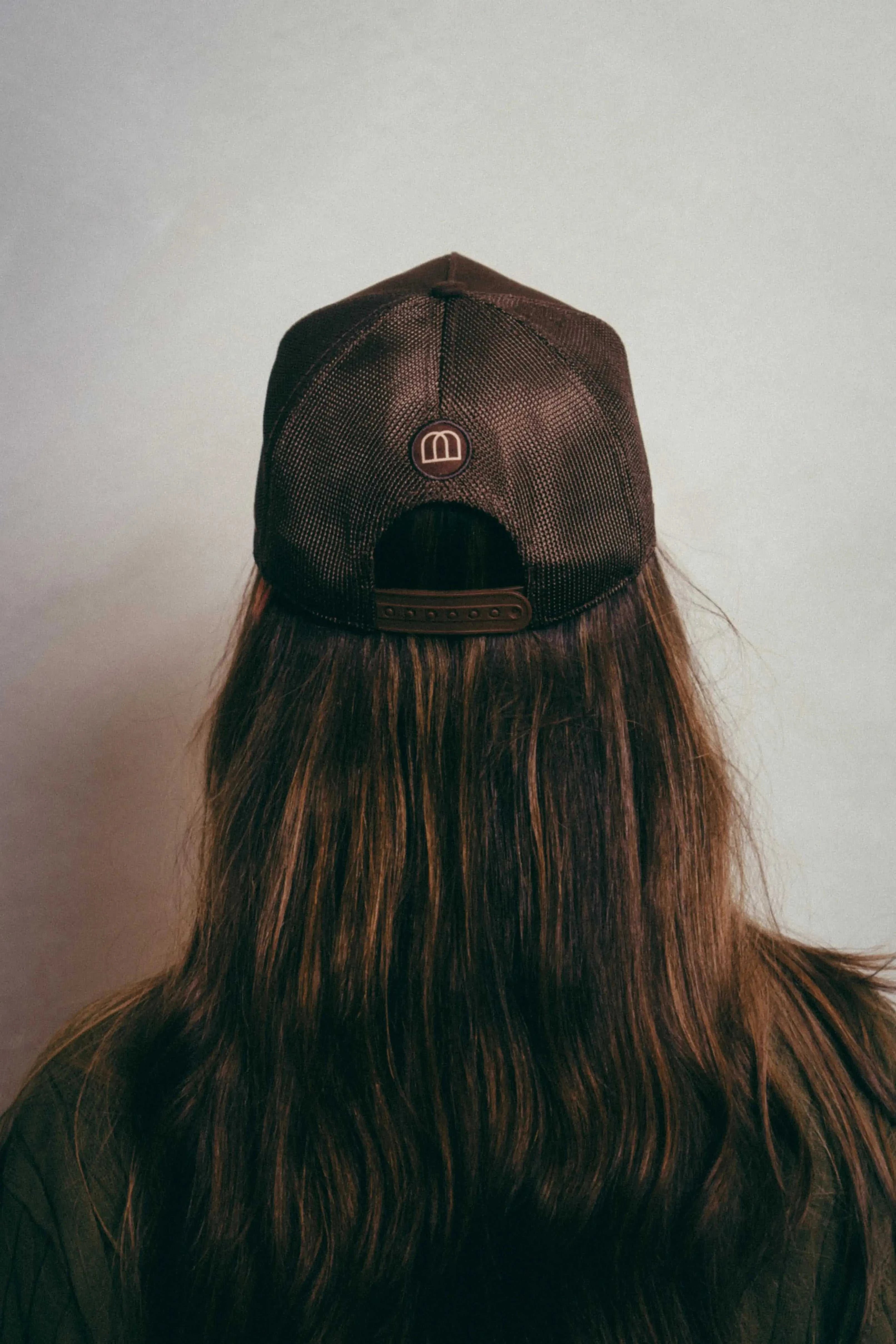 Back view of brown Ovals Mesh-Back Trucker Hat on person with long hair