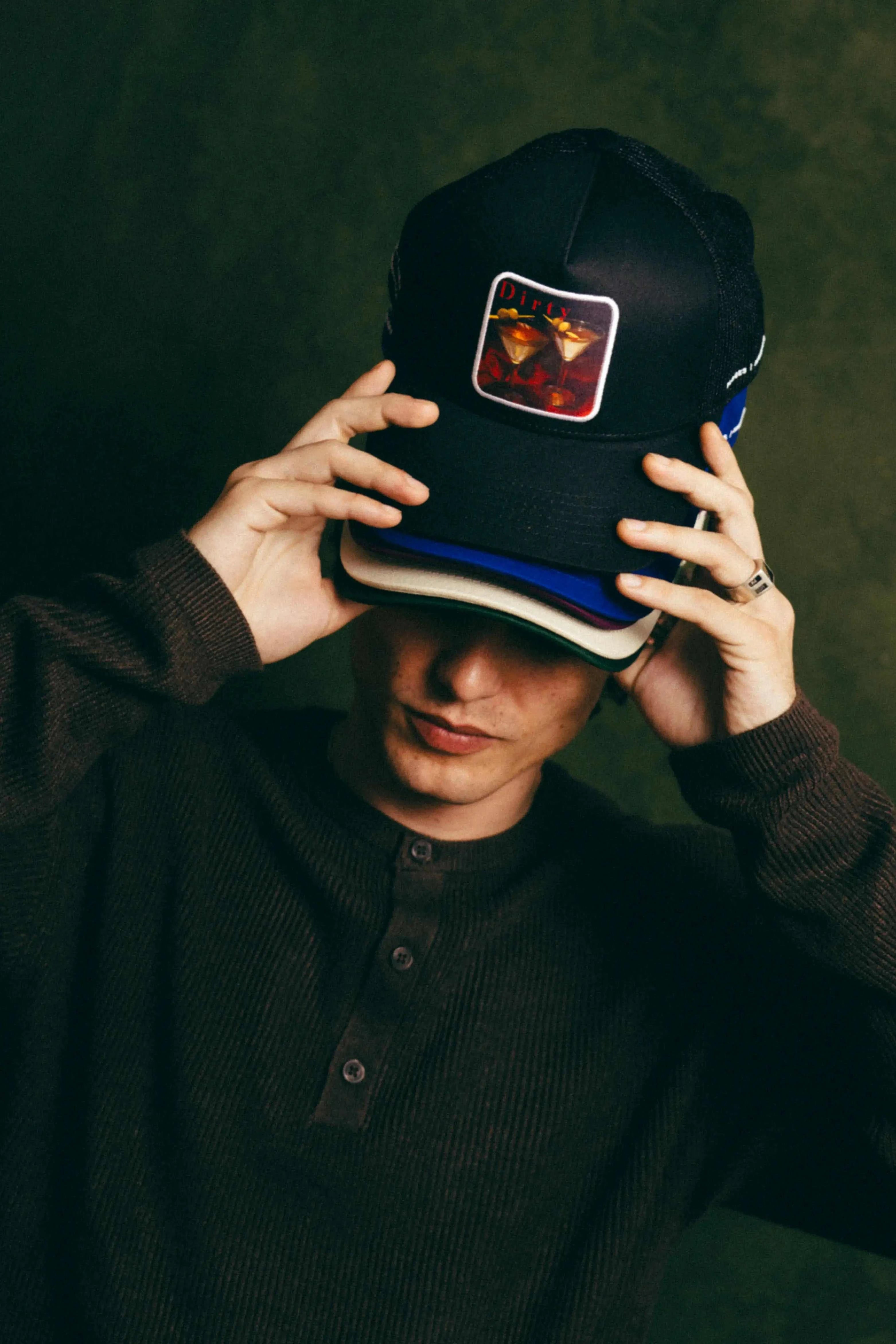 Dirty Martini Trucker Hat in black with mesh back and signature patch worn by person adjusting hat